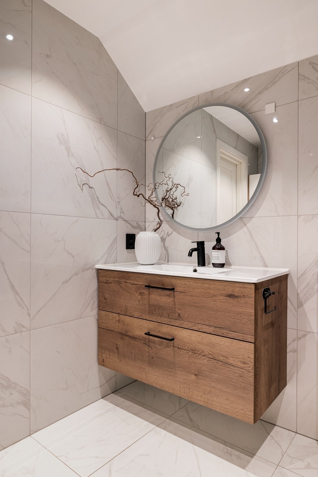 Rommet er utstyrt med et stilrent servantskap med nedfelt servant, ovalt speil med innebygd berøringslys, og vegghengt klosett med innebygd sisterne. Galleribilde