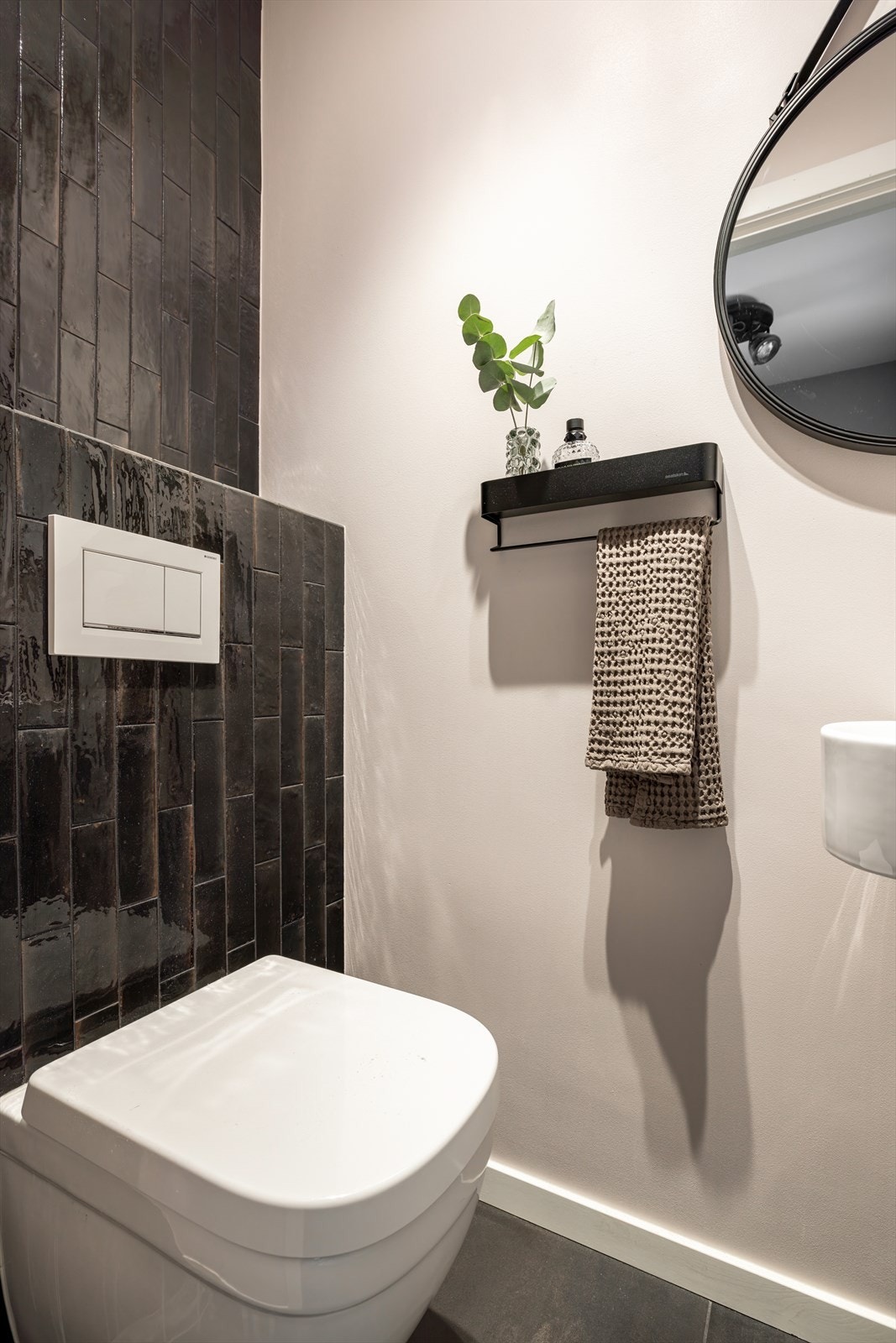 Rommet er utstyrt med servant med sort og messingfarget armatur og vegghengt klosett. Det er elektriske varmekabler i gulvet og mekanisk avtrekk. Galleribilde