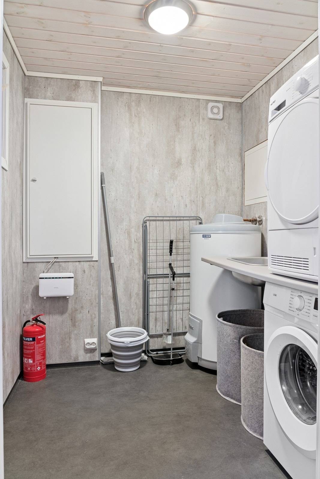Praktisk vaskerom med belegg på gulv og våtromsplater på veggene. Rommet har skyllekar nedfelt i benkeplate og opplegg for vaskemaskin. Galleribilde