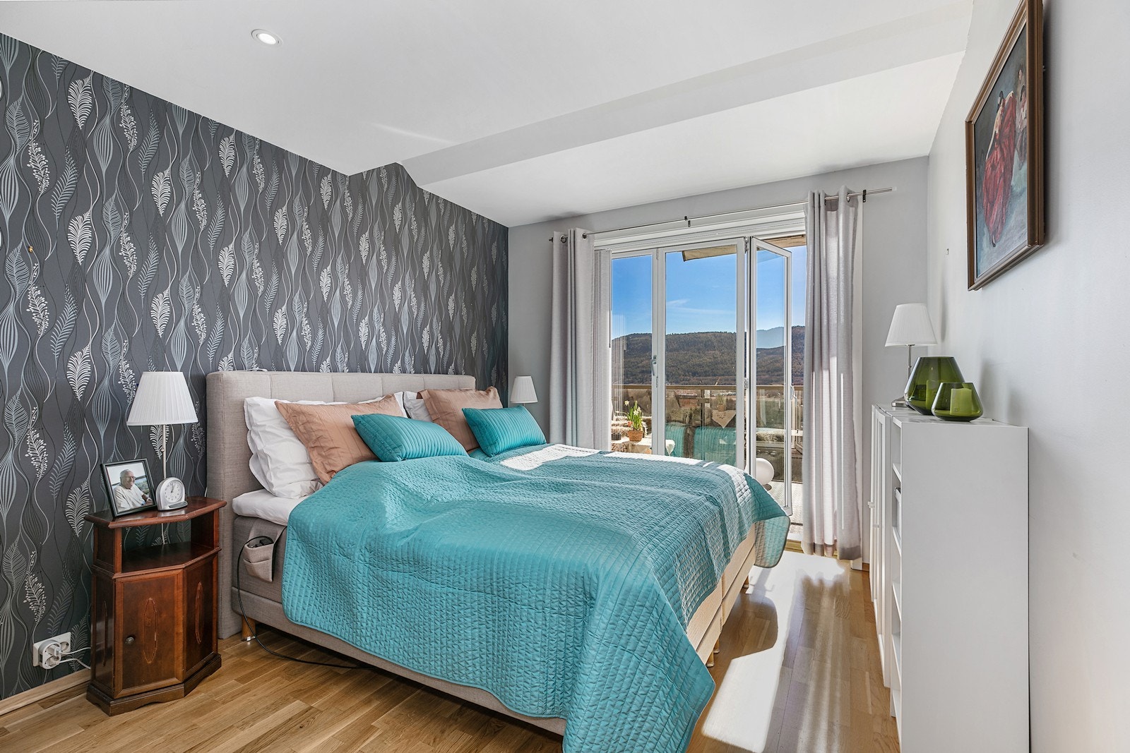 Lyst og romslig hovedsoverom med tapetsert kontrastvegg og parkett på gulv. Galleribilde