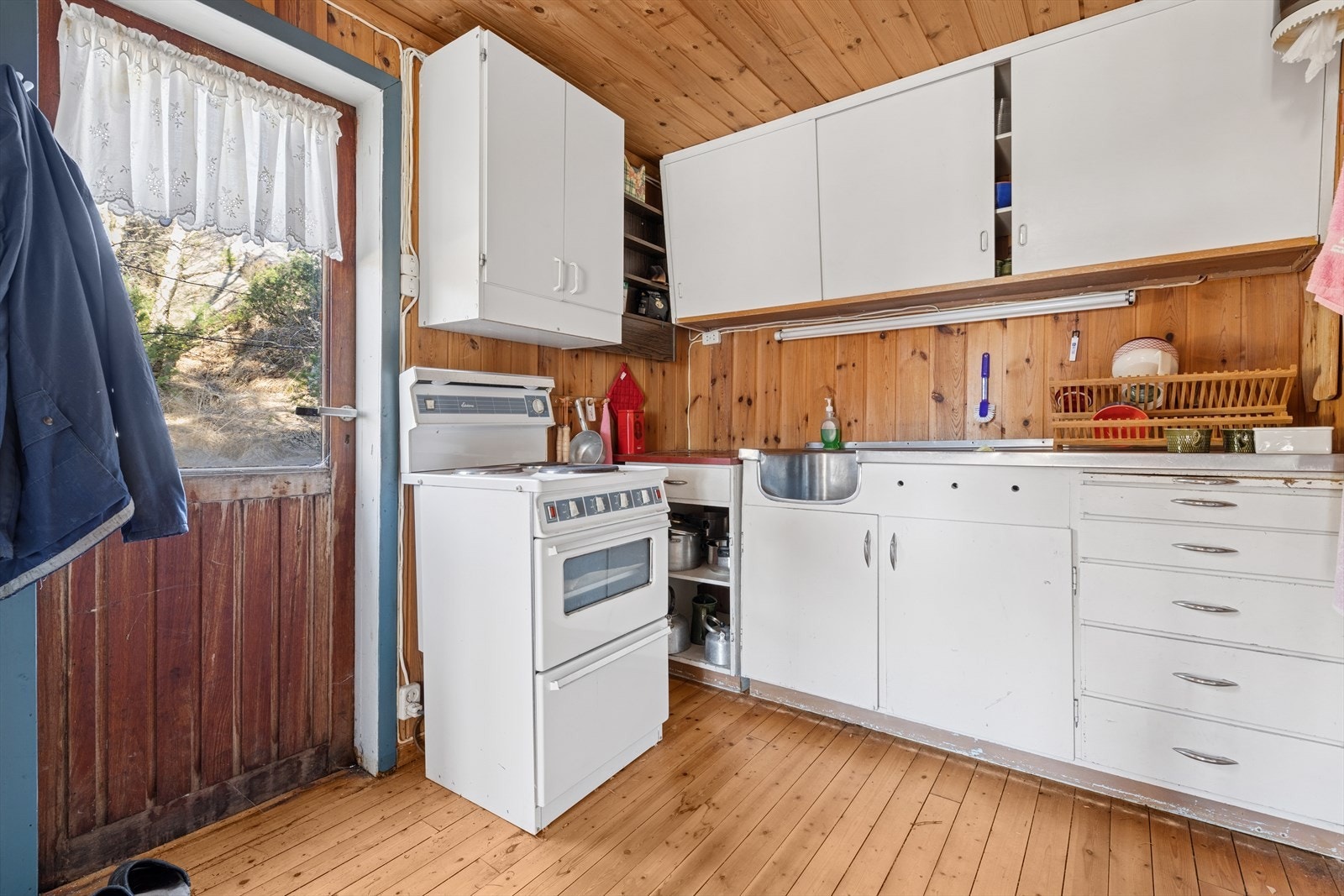 Kjøkkenet har en eldre innredning med overskap med glatte fronter og kjøkkenbenk med kjøkkenkum i stål. Galleribilde