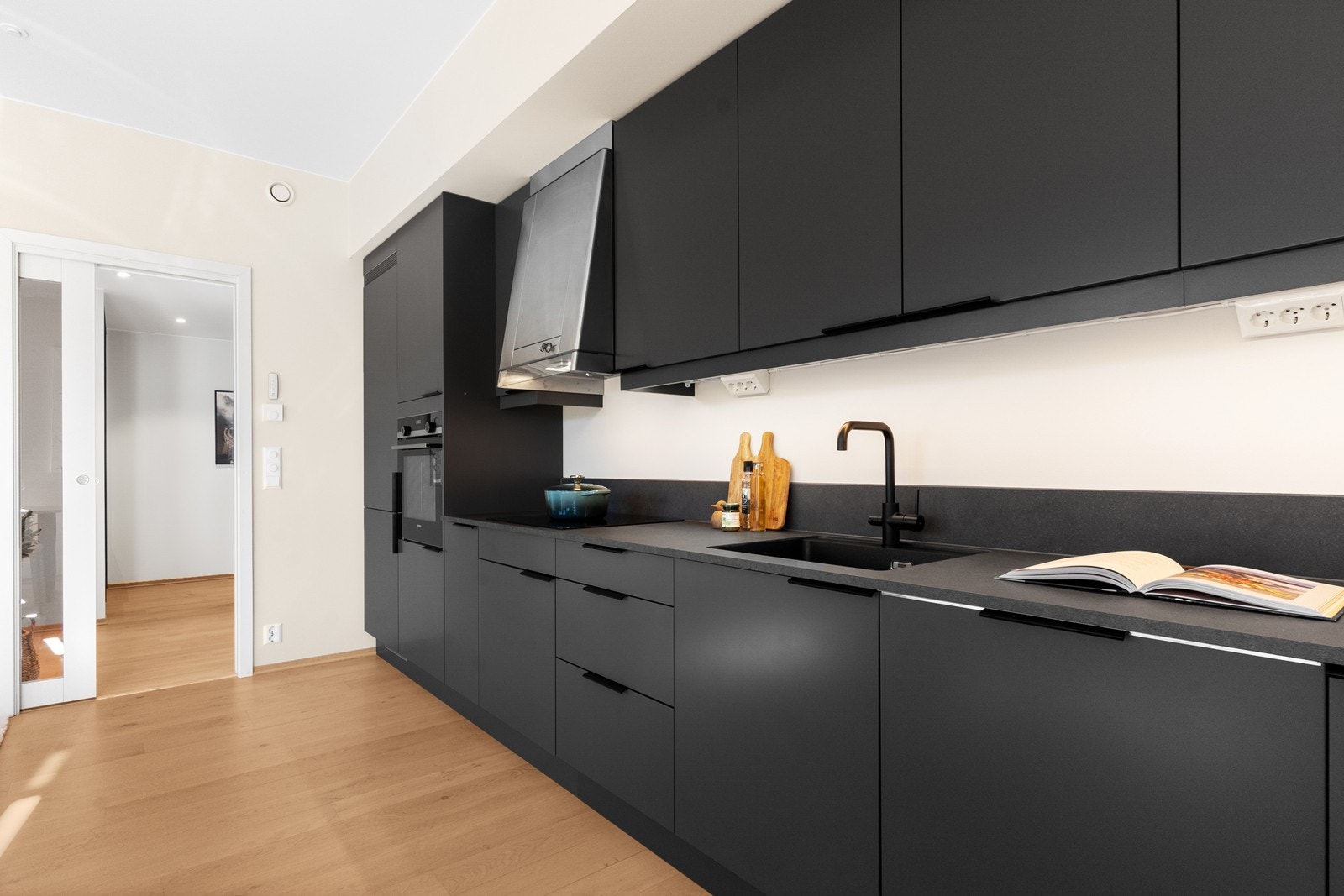 Kjøkkenet har alt man trenger funksjonelt plassert på én vegg i det åpne rommet, med innredning i over- og underskap. Galleribilde