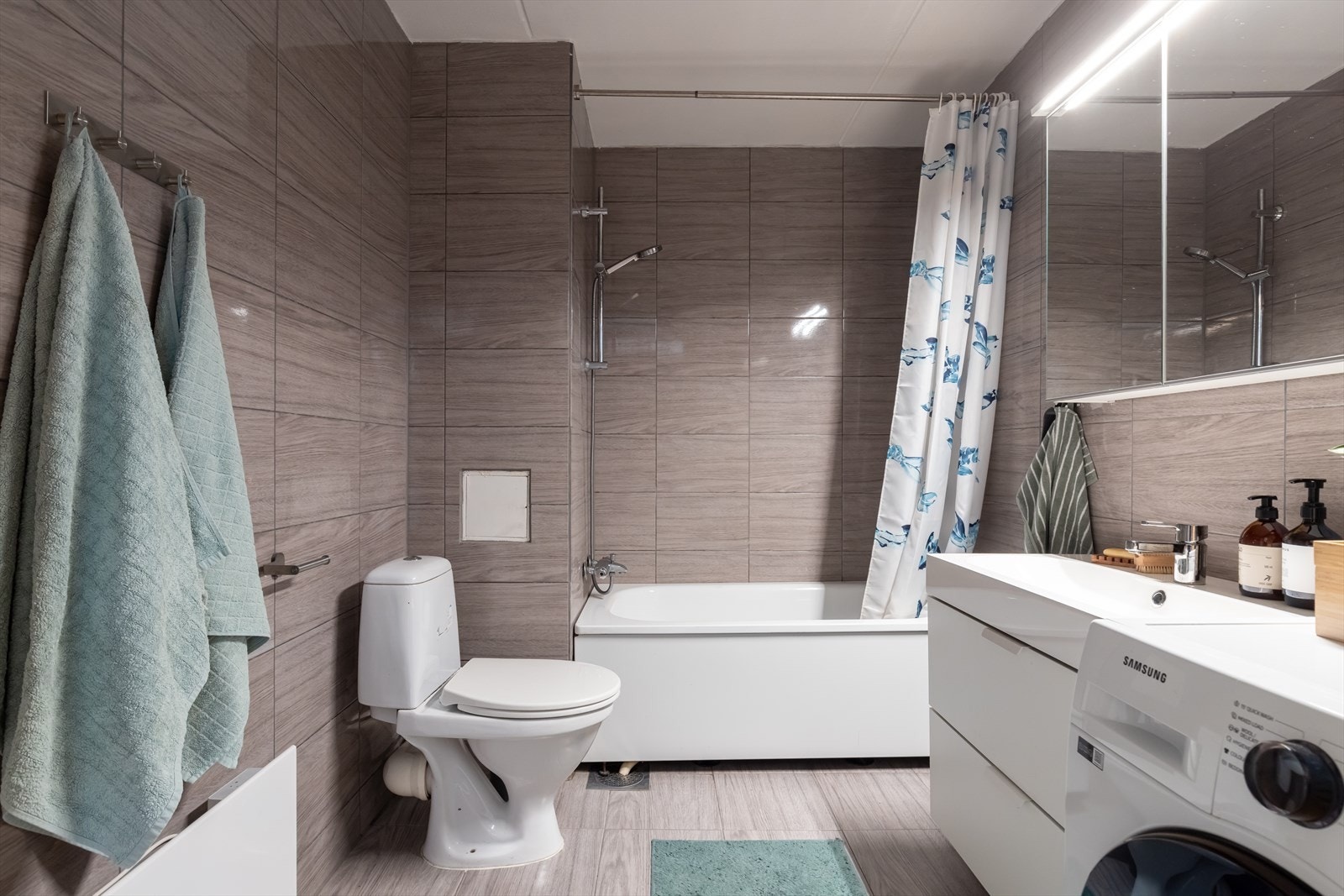 Badet er innredet med benkeskap med glatte fronter, gulvstående klosett, servant, dusj i badekar og opplegg for vaskemaskin. Galleribilde