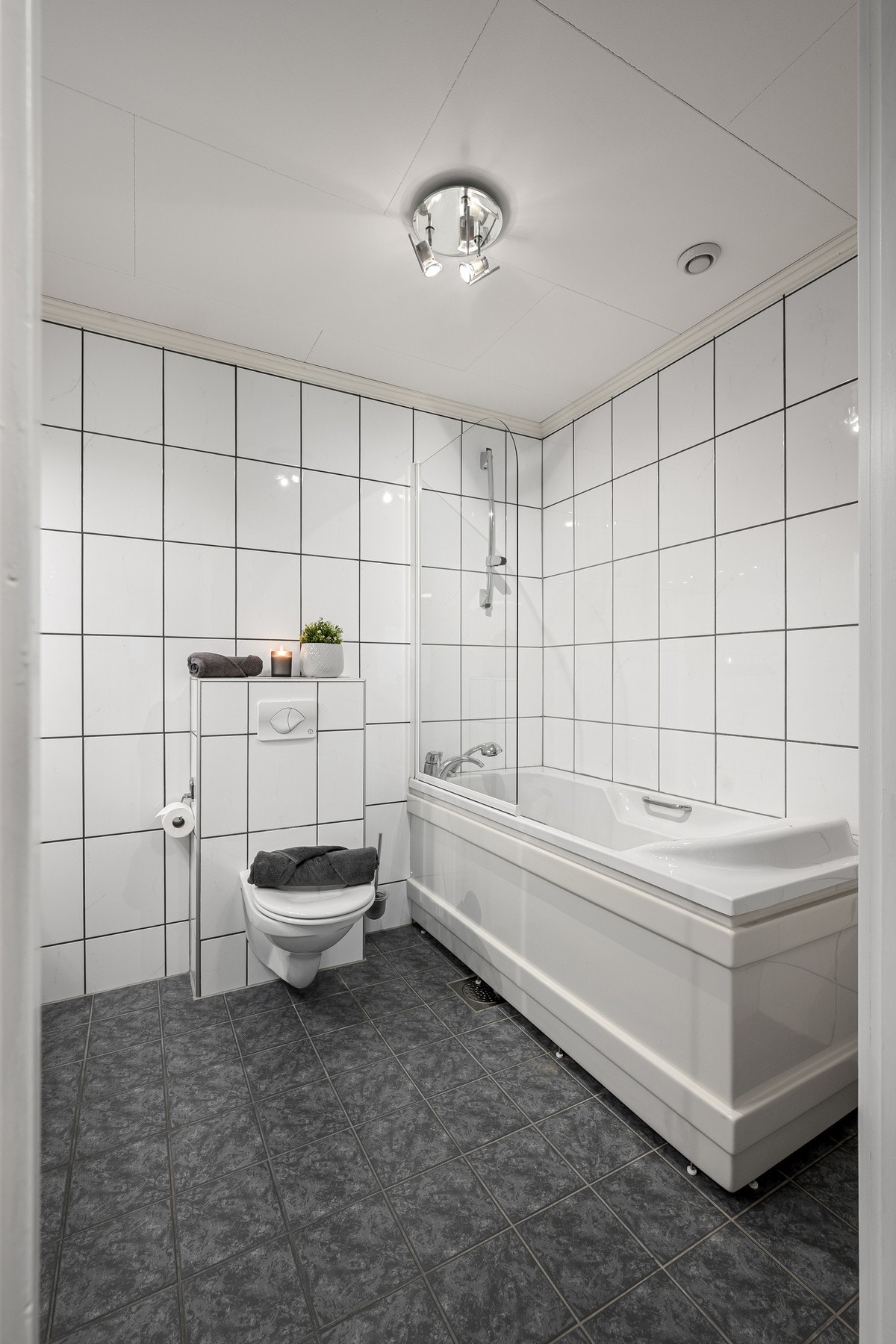 Badet er utstyrt med vegghengt toalett, stor innredning og badekar med dusjvegg Galleribilde