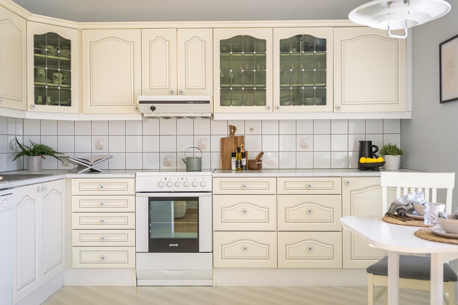 Innredning med profilerte lakkerte fronter, laminat benkeplate med fliser på bakvegg, dobbel rustfri oppvaskkum, ventilator med kullfilter og frittstående hvitevarer som komfyr, oppvaskmaskinen og kjøl/frys Galleribilde