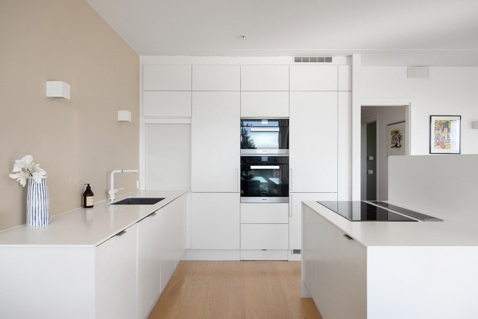 De hvite, glatte frontene gir et stilrent uttrykk, og innredningen består av kjøkkenøy, høyskap og underskap. Galleribilde