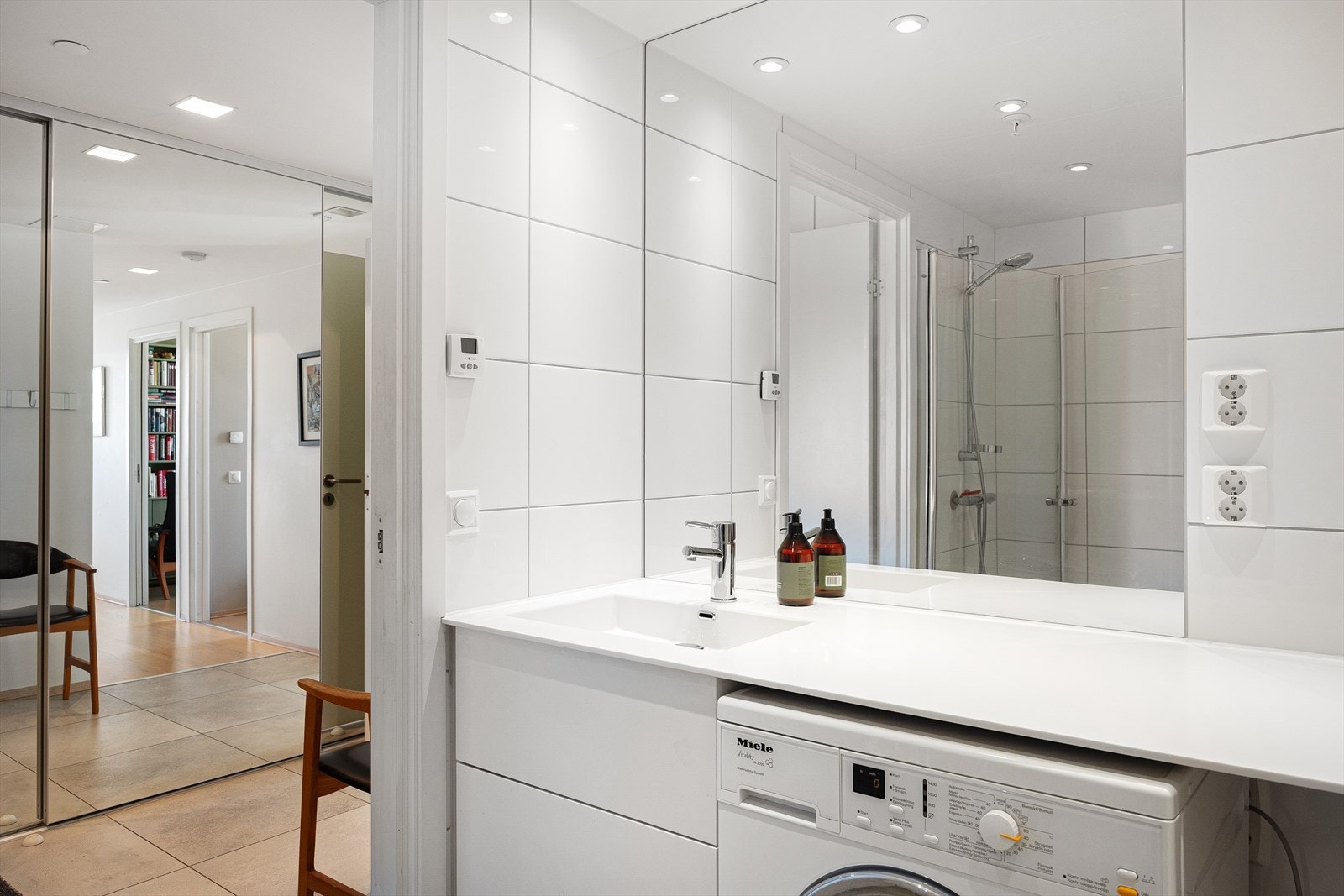 Badet består av benkeplate med servantskap og nedfelt servant, innmurt speil, vegghengt klosett, og dusjhjørne med svingdører i herdet glass. Opplegg vaskemaskin. Galleribilde