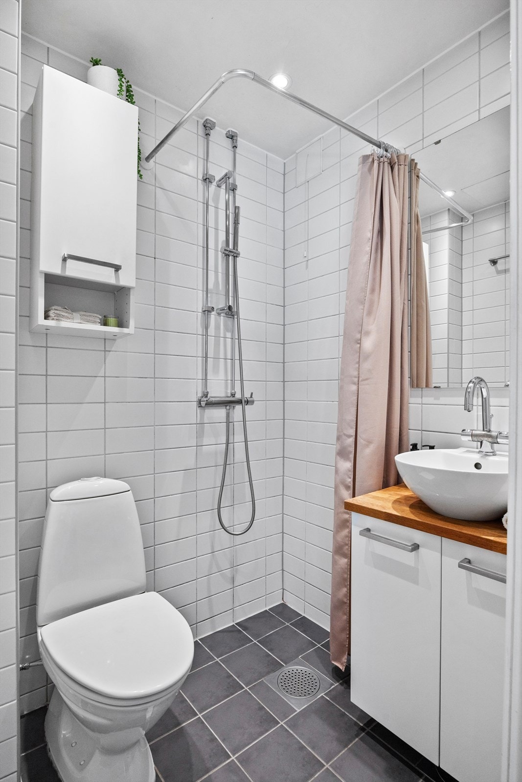 Flislagt bad med gulvvarme - utstyrt med servantskap, dusjhjørne med forheng og gulvstående toalett Galleribilde