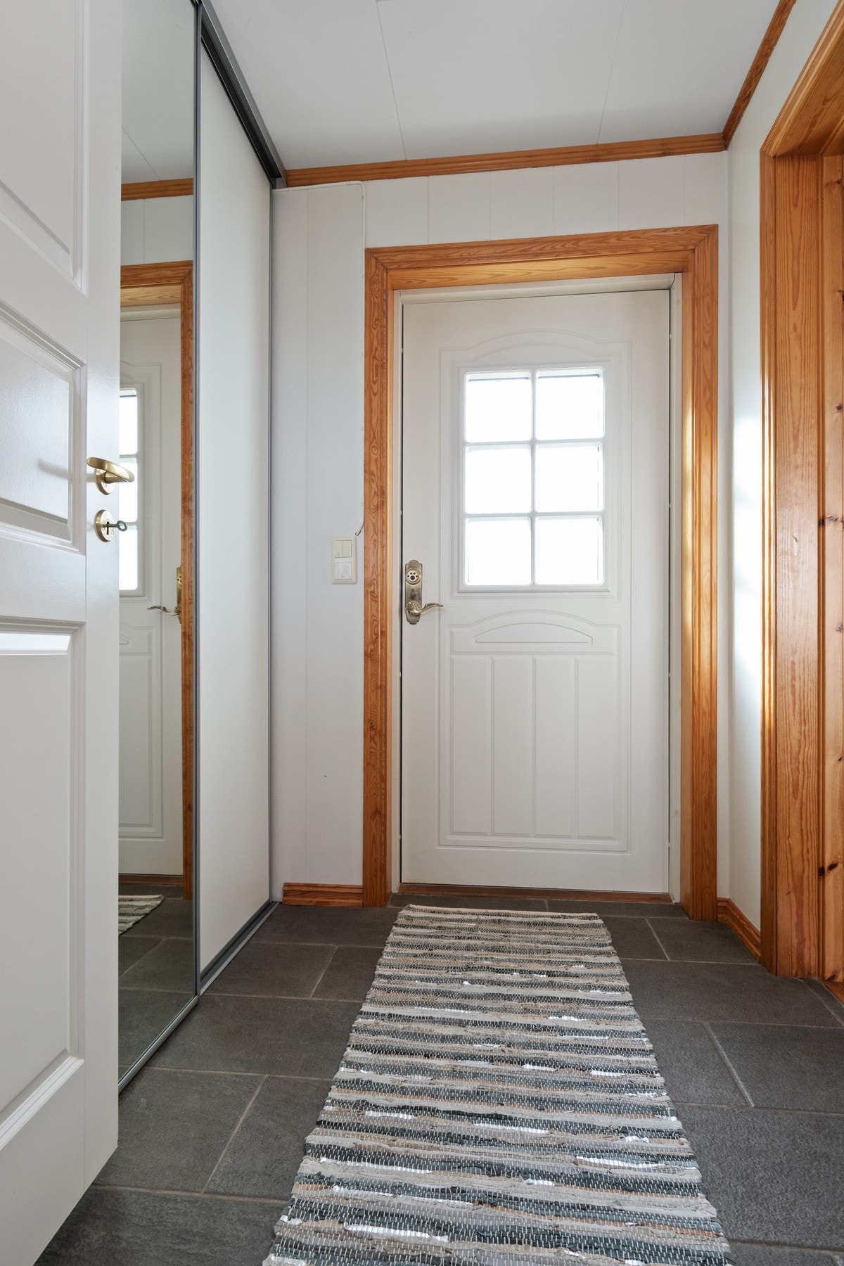 Vel inne blir vi ønsket velkommen i en fin entré med hvitmalte vegger og grå fliser på gulv med gulvvarme. Yttertøy, sko og utstyr ryddes enkelt bort i en romslig, plassbygd skyvedørsgarderobe. Galleribilde