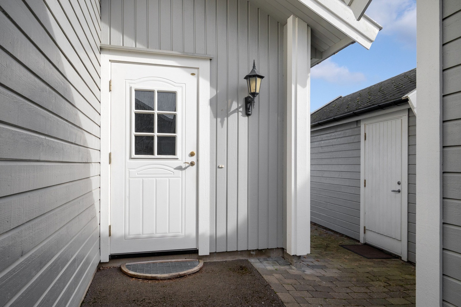 Boligen har et pent inngangsparti med steinbelagt adkomst og veggmontert, klassisk utebelysning. Galleribilde