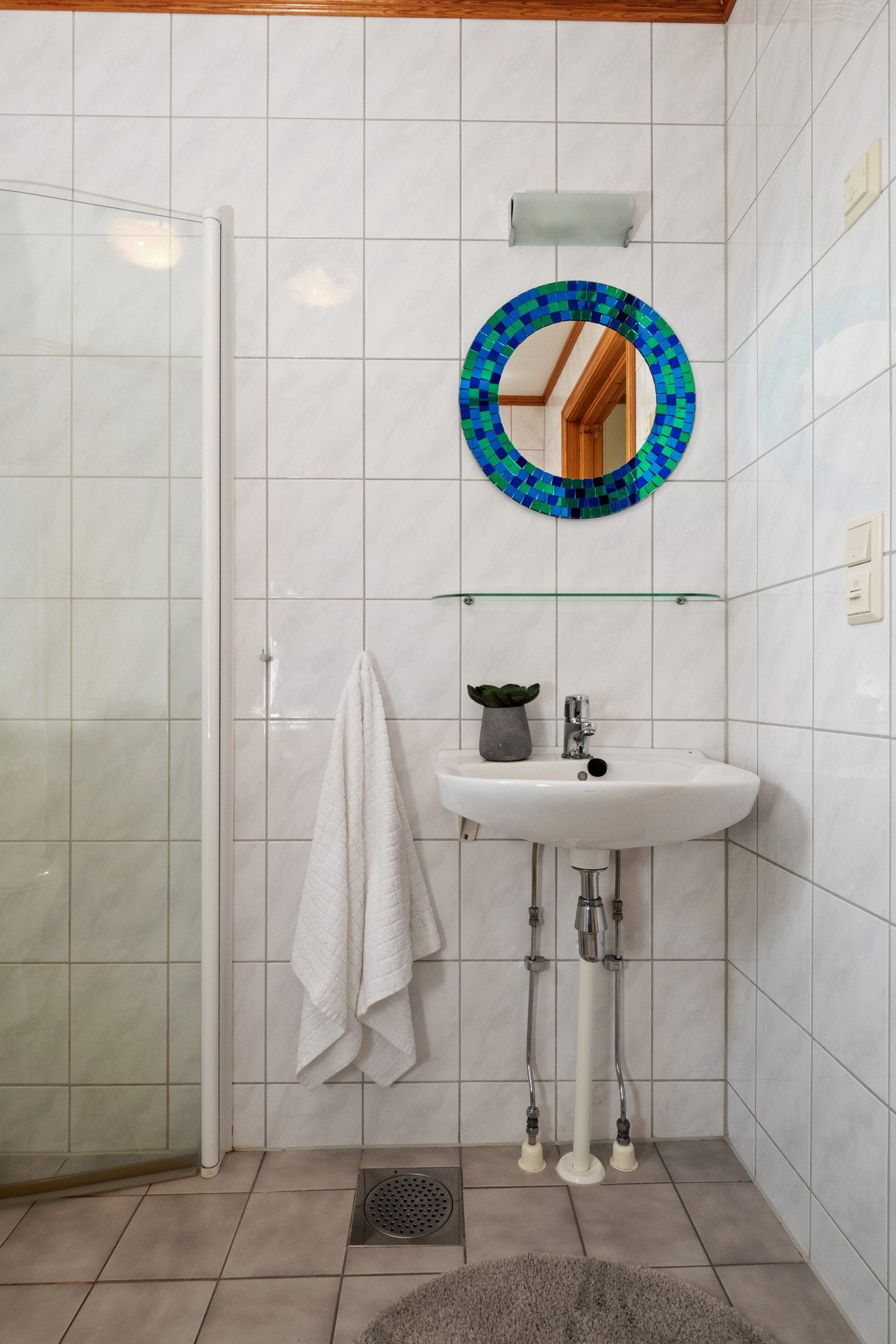 Av innredning er det servant, hylle, speil og belysning, og badet er videre utstyrt med toalett, mekanisk avtrekk, opplegg for vaskemaskin og et dusjhjørne med innfellbare glassdører. Galleribilde