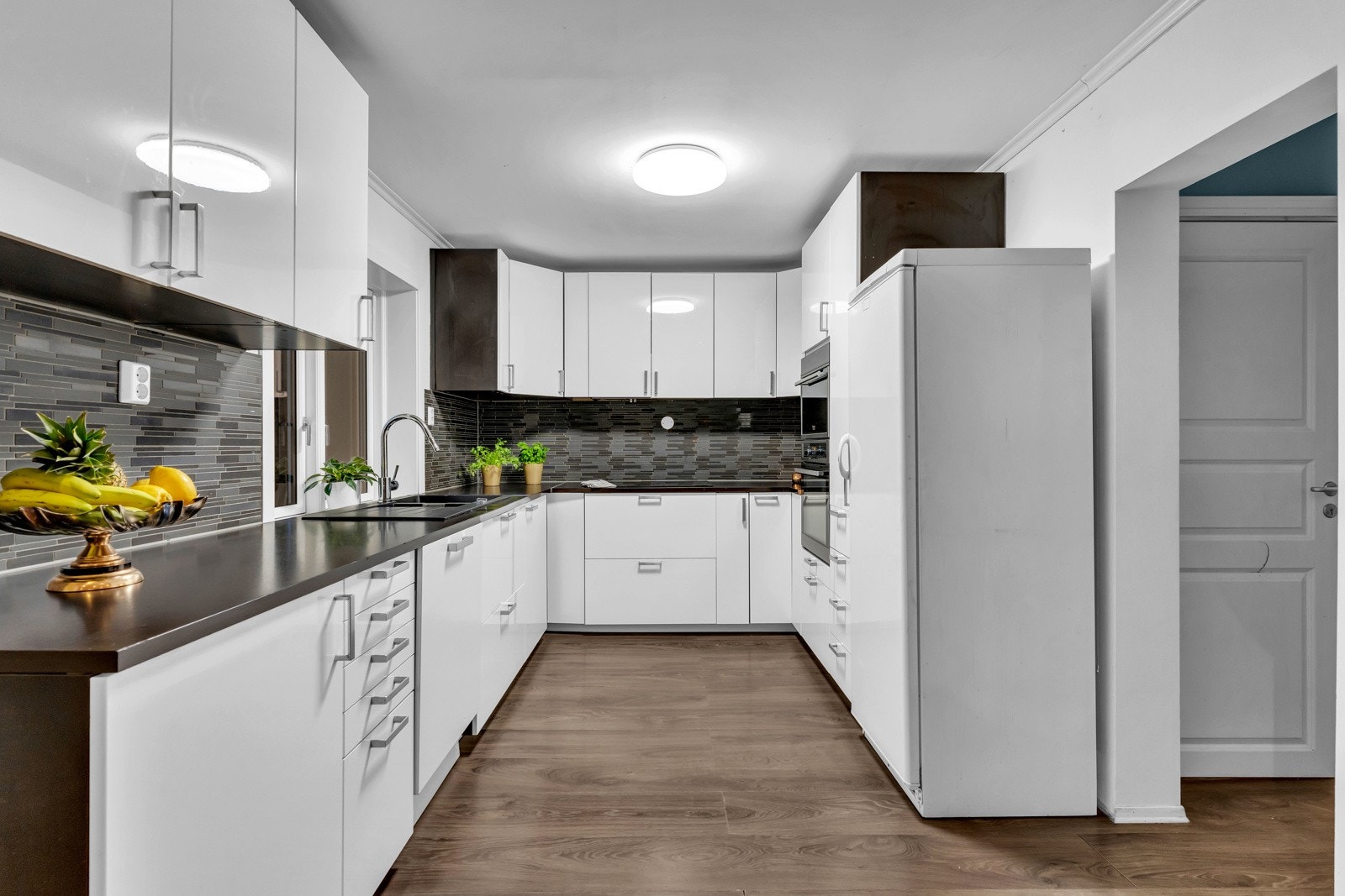 Tidløst kjøkken med lyse fronter og en mørkere benkeplate. Galleribilde