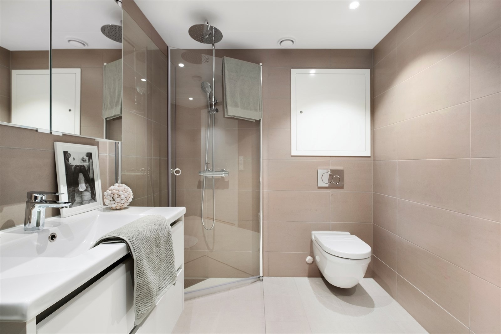 Badet er utstyrt med åpen dusjløsning med praktiske innfellbare glassdører, baderomsinnredning med speilskap og servant, opplegg for vaskemaskin, veggmontert wc og downlights. Galleribilde