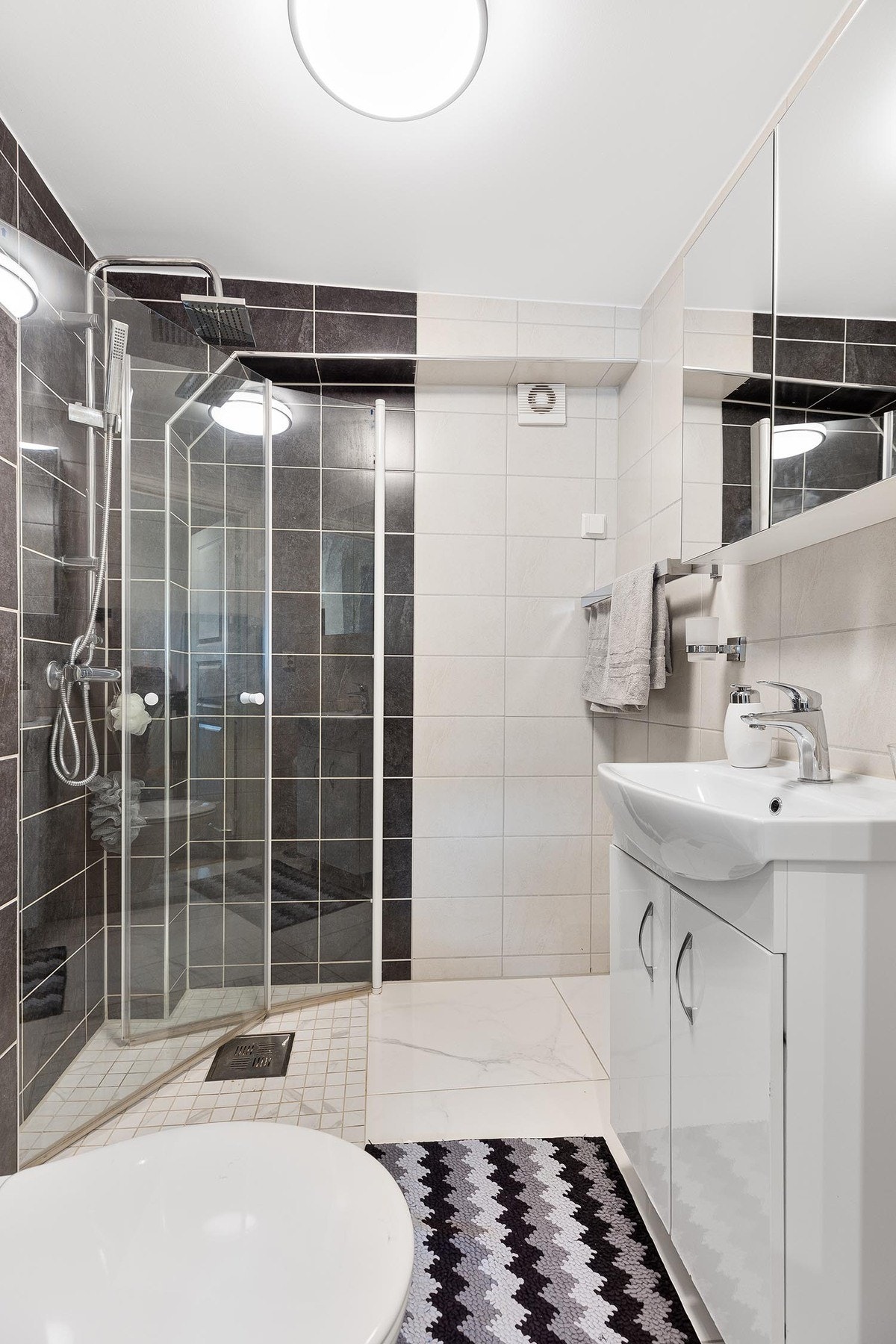 Badet er stilfullt med en kombinasjon av lyse og sorte fliser på gulv og vegger. Galleribilde