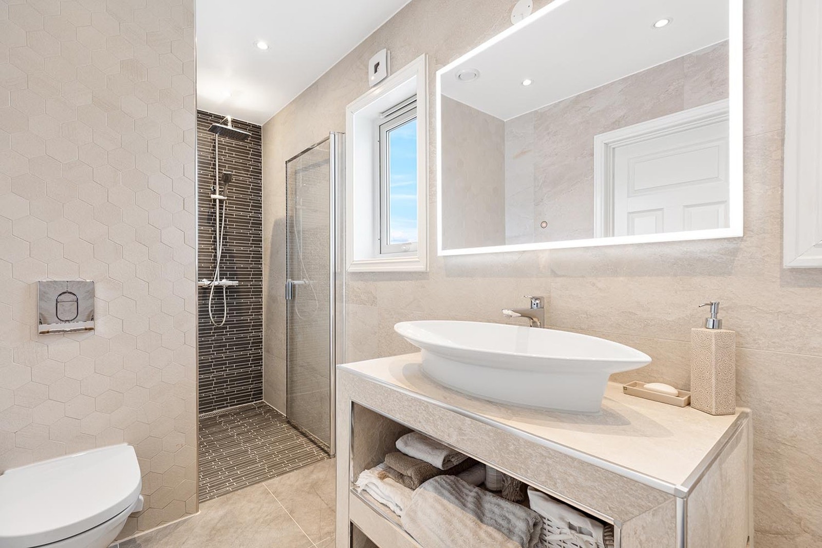 Dusjen er plassert i en egen nisje med kontrastfliser, herdet glassdør, og regnfallsdusj. Galleribilde