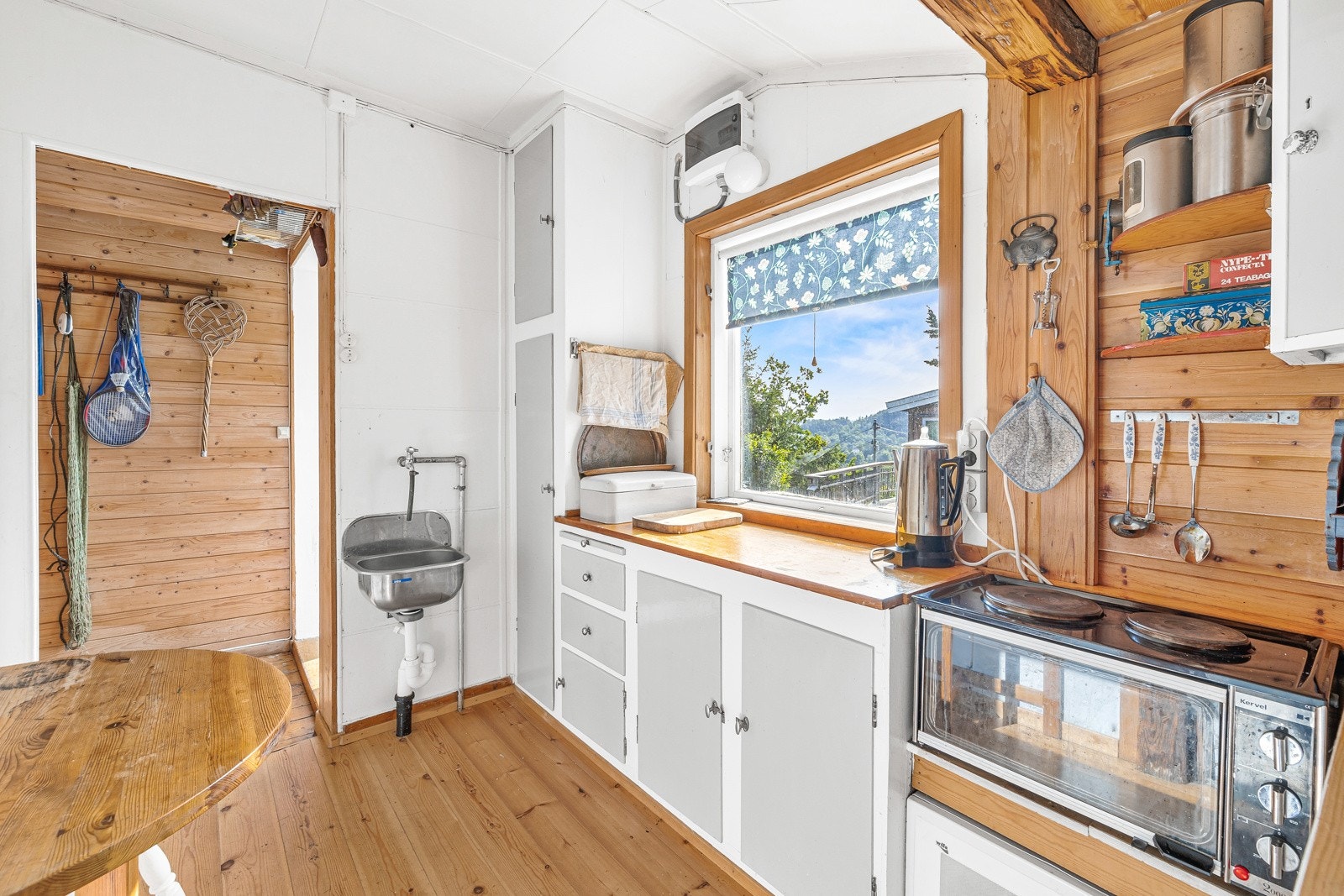 Kjøkken med slette fronter og benkeplater av heltre. Frittstående kjøleskap i vegg, og koketopp og mikrobølgeovn i benk. Galleribilde