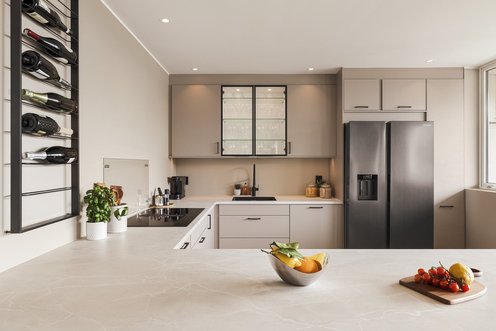 Ett av overskapene har en elegant glassfront, som tilfører et luftig preg til rommet. Benkeplaten er i slitesterkt laminat, og over den er veggflatene malt for en helhetlig og harmonisk finish Galleribilde