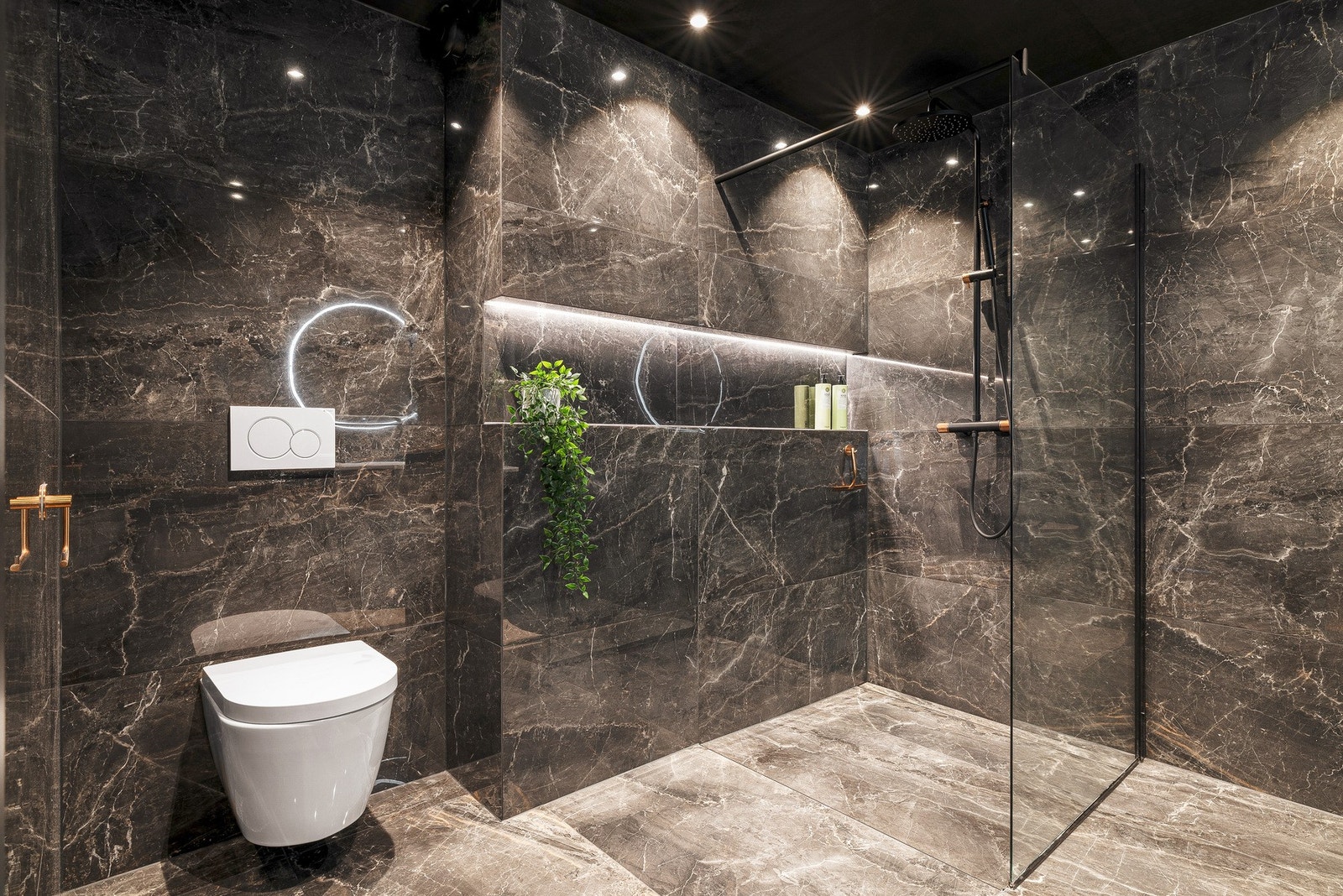 Rommet er utstyrt med et vegghengt toalett, helstøpt servanten, speil med integrert lys og dusj med vegger i klart glass Galleribilde