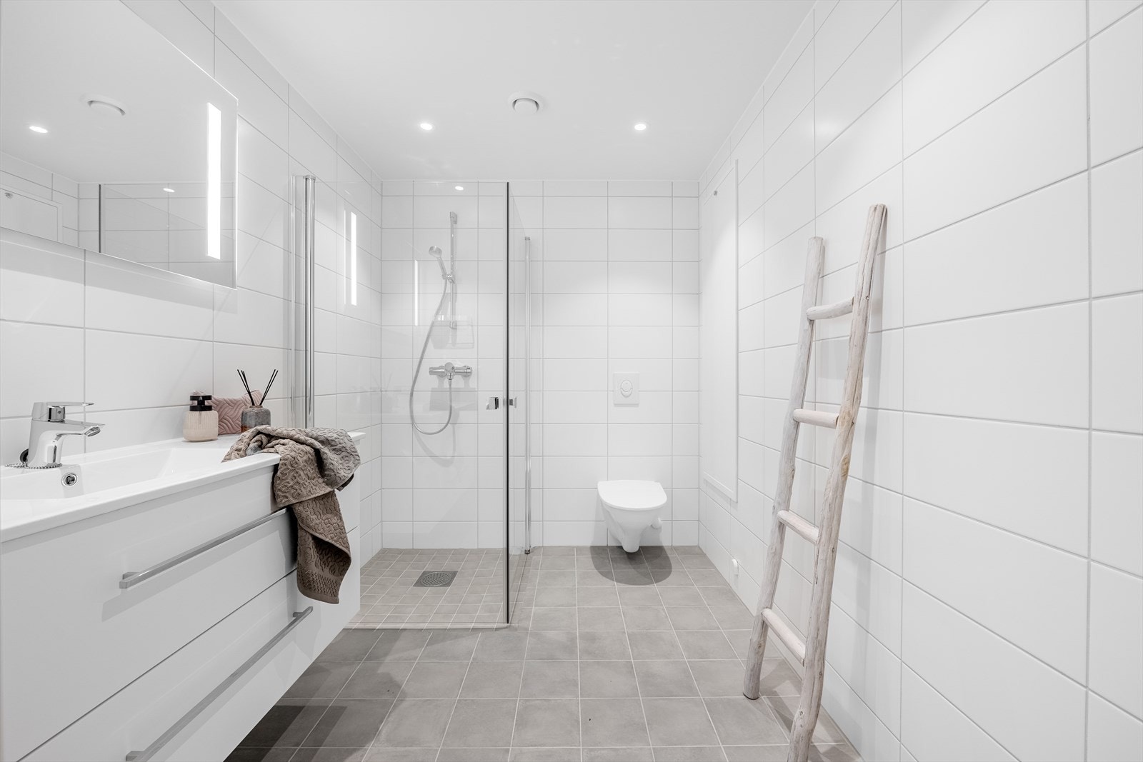 Helfliset baderom med vegghengt wc, dusj, og servant med oppbevaring. Galleribilde