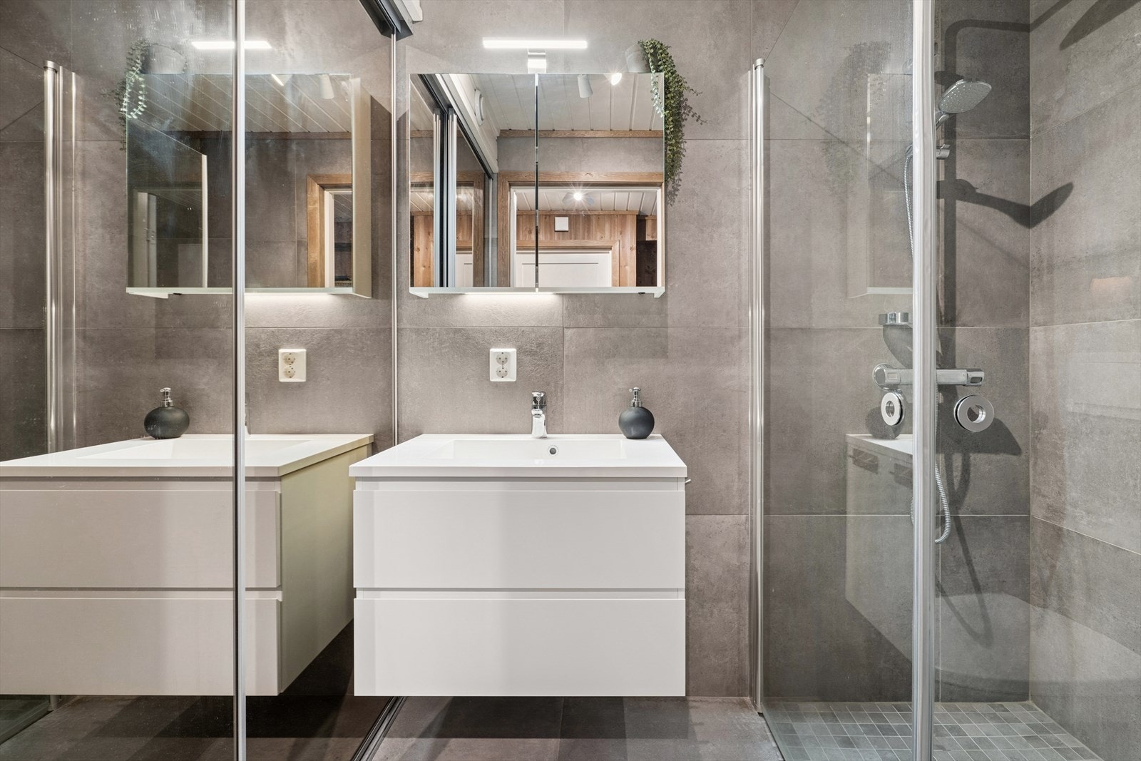 Badet er innredet med et veggmontert toalett, baderomsinnredning med heldekkende servant, speilskap med overliggende belysning og dusj med innfellbare dusjdører. Galleribilde