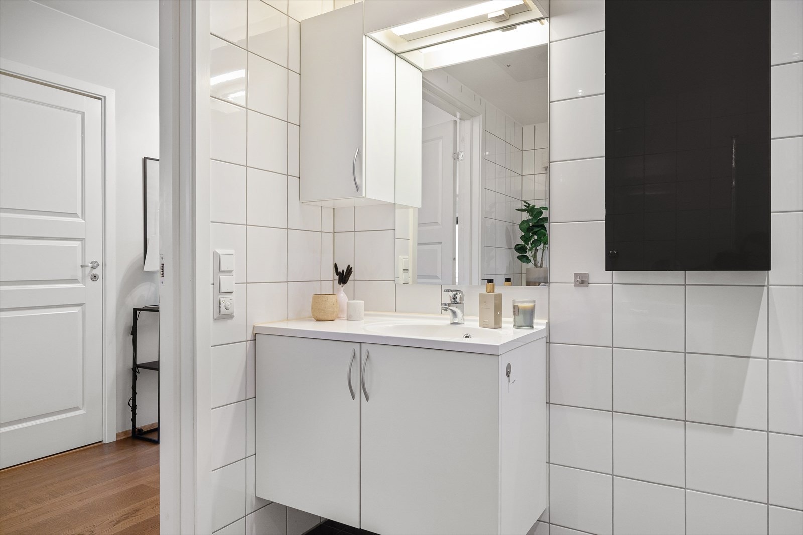 Badet har et praktisk servantskap med servant, veggskap med lys over, vegghengt toalett og dusjsone med dusjdører. Det er også opplegg for vaskemaskin. Galleribilde