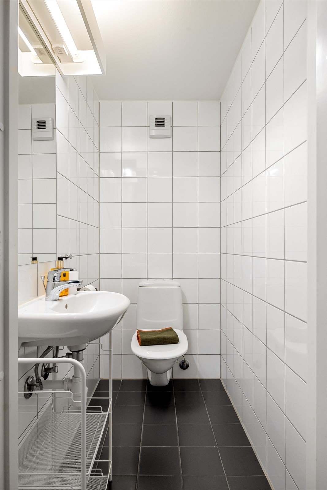 Praktisk, flislagt toalettrom med vegghengt WC og servant. Galleribilde