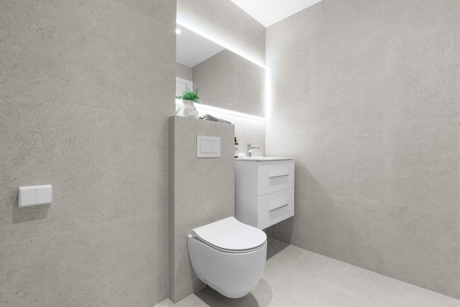 Innredningen består av servant i skuffeseksjon med 1-greps blandebatteri, speil med sminkelys, vegghengt wc og dusjhjørne med glassdører Galleribilde