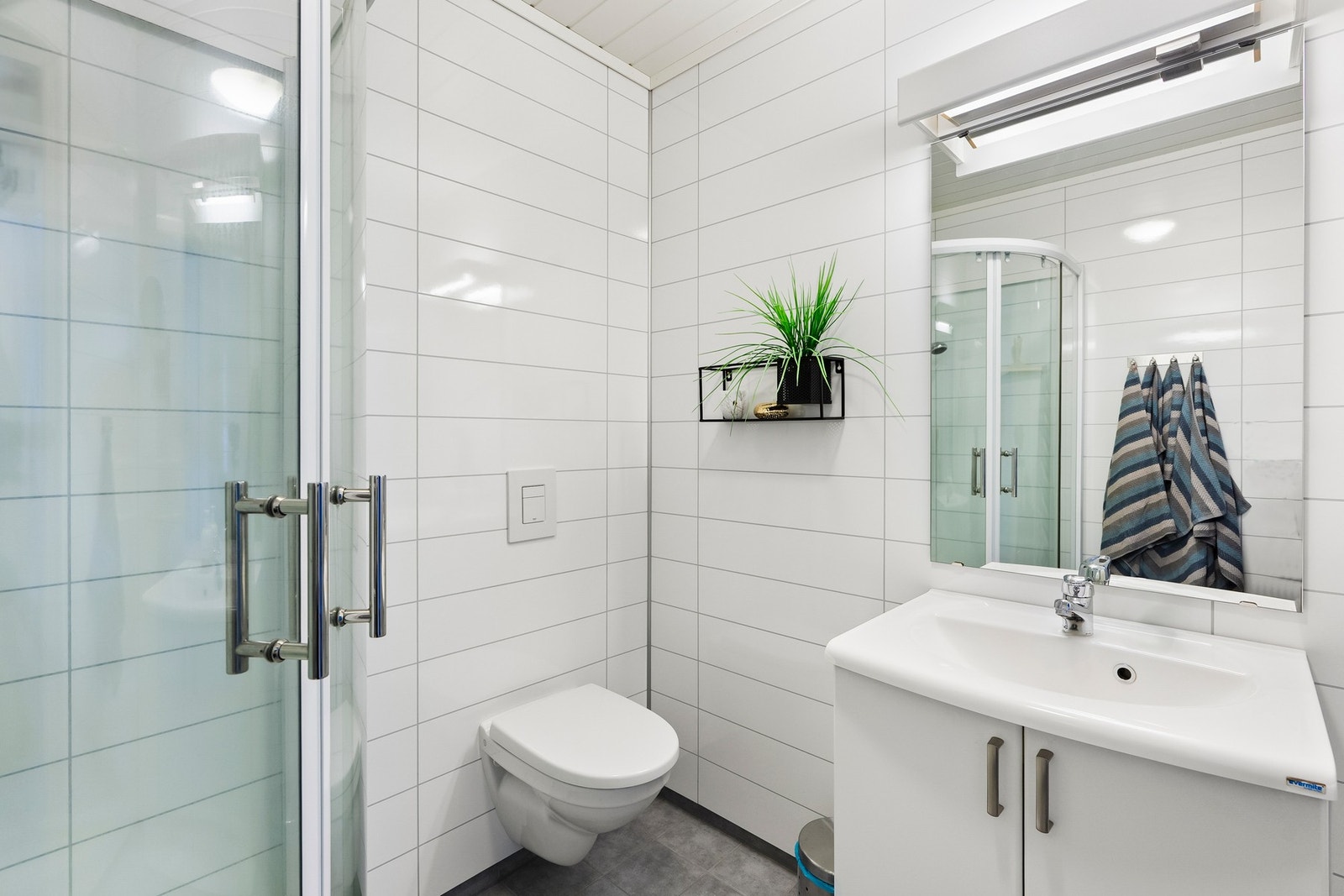 Vask med underskap for oppbevaring, et vegghengt toalett som letter rengjøringen, og et dusjkabinett. Galleribilde