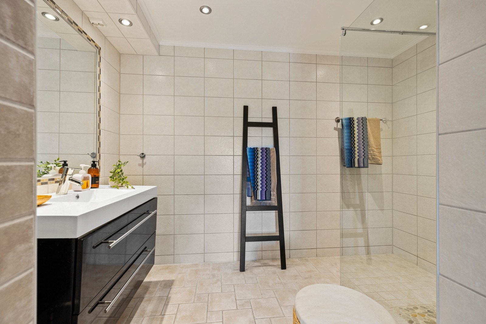 Badet har fliser på vegger og gulv, dusjhjørne med glassvegg, og moderne servant med underskap Galleribilde