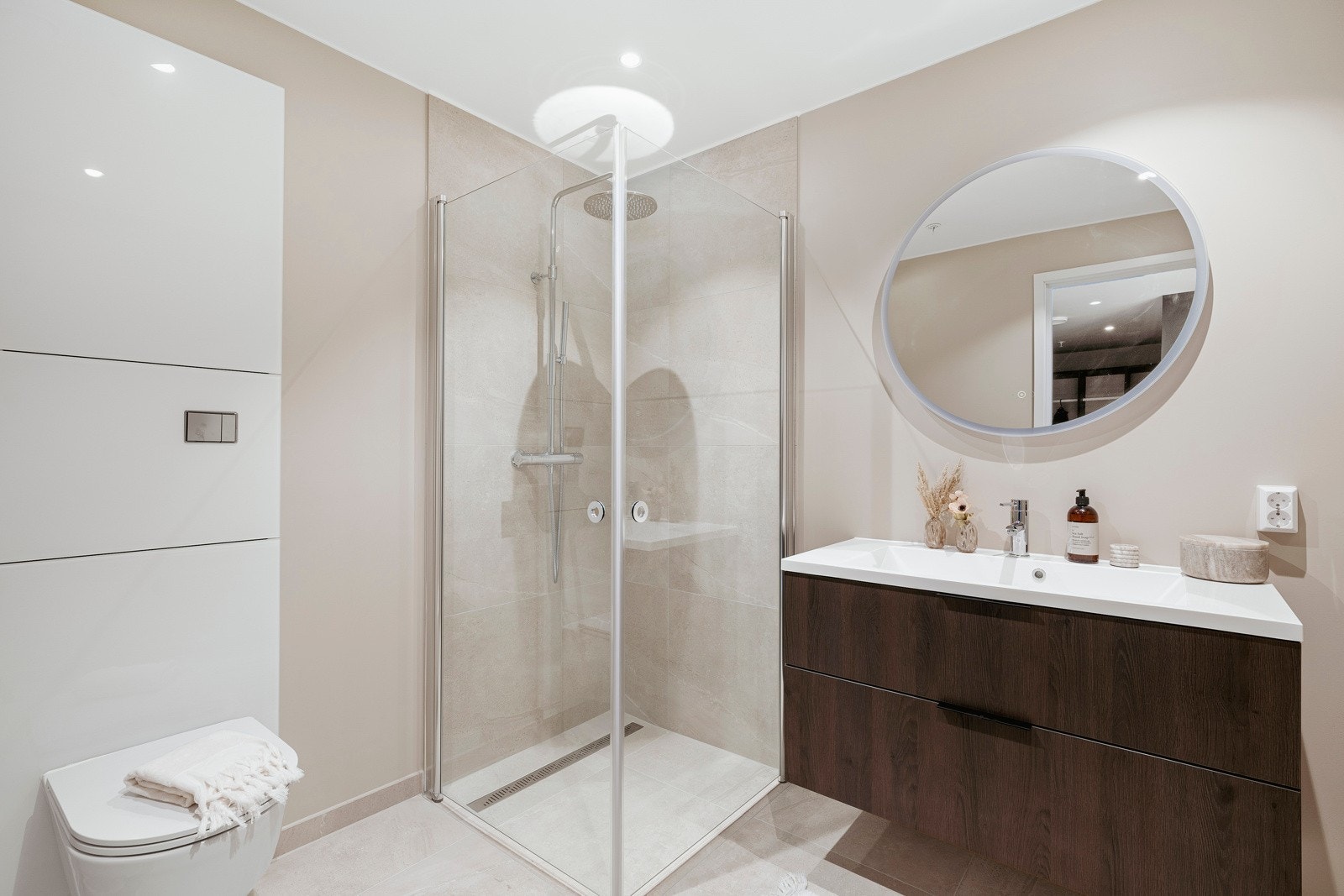 Badene er stilrene med delikate materialvalg og en moderne finish, der store, beige gulvfliser kombineres med matchende fliser og duse flater på veggene. Galleribilde