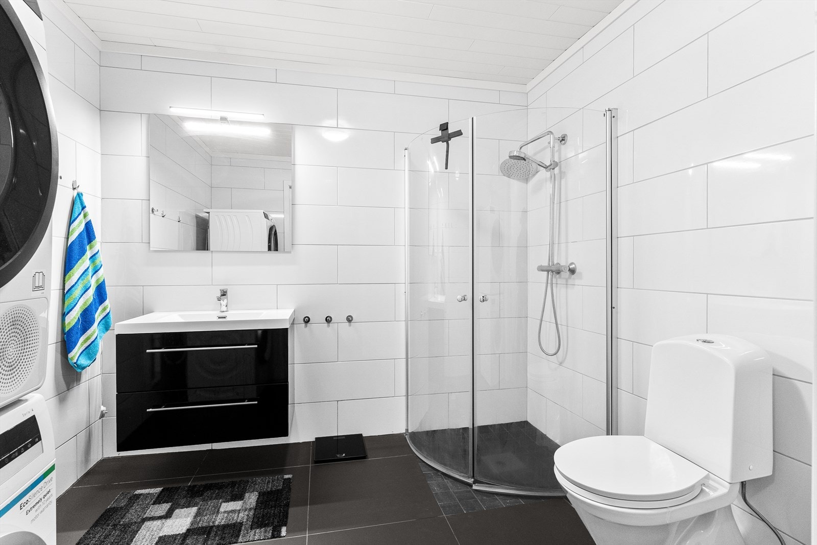 Badet i underetasjen er stilrent innredet med sort servantinnredning med enkel servant og speil med belysning. badet er utstyrt med toalett, dusjhjørne med innfellbare dusjvegger og opplegg for vaskemaskin og tørketrommel. Galleribilde