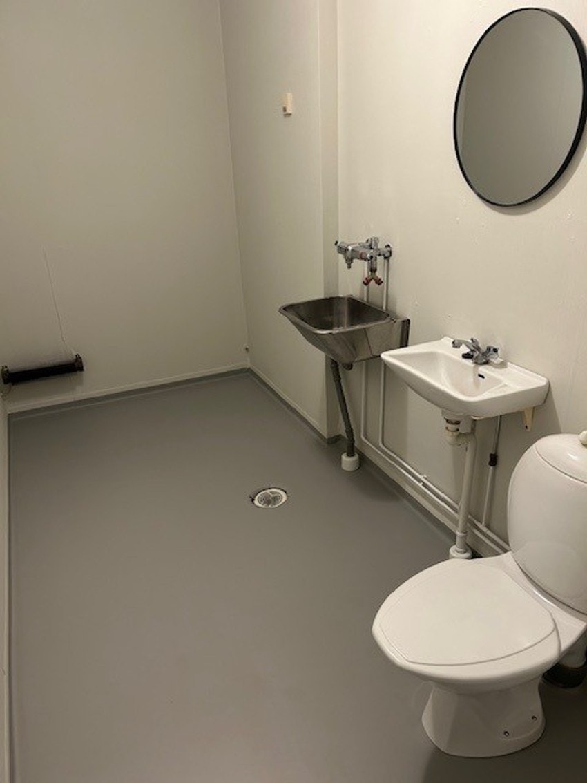 Kombinert bad og vaskerom med belegg på gulv og tapet vegg. Rommet er innredet med gulvmontert klosett, vask med speil, utslagsvask og opplegg til vaskemaskin. Galleribilde