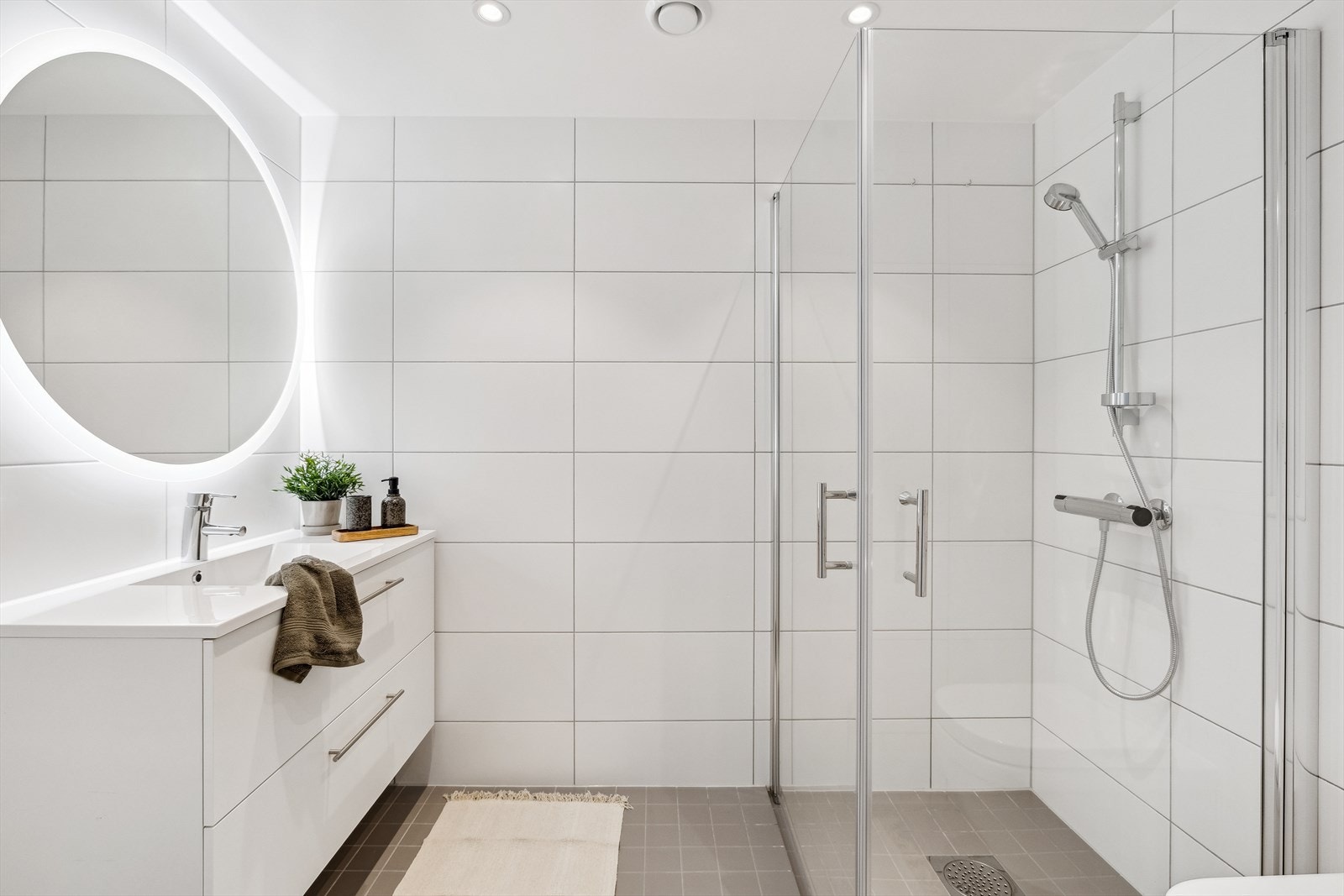 Romslig fliselagt baderom med dusjnisje, servant, speil med lys og WC Galleribilde