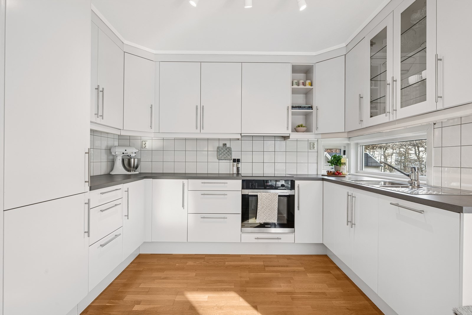 Kjøkkenet er lyst og moderne med hvite slette fronter, hvite backsplash fliser. Fult utstyrt med stekeovn, platetopp, oppvaskmaskin og kjøleskap Galleribilde