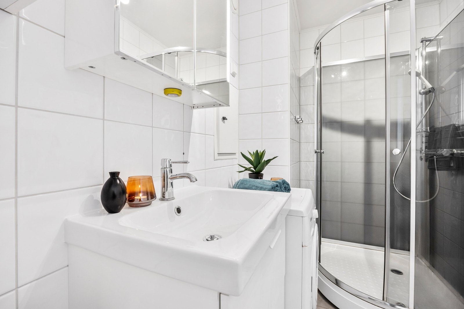 Innredningen består av en servant, speilskap med belysning og overskap for praktisk oppbevaring. Videre har badet et frittstående toalett og et dusjkabinett. Det er opplegg for vaskemaskin Galleribilde