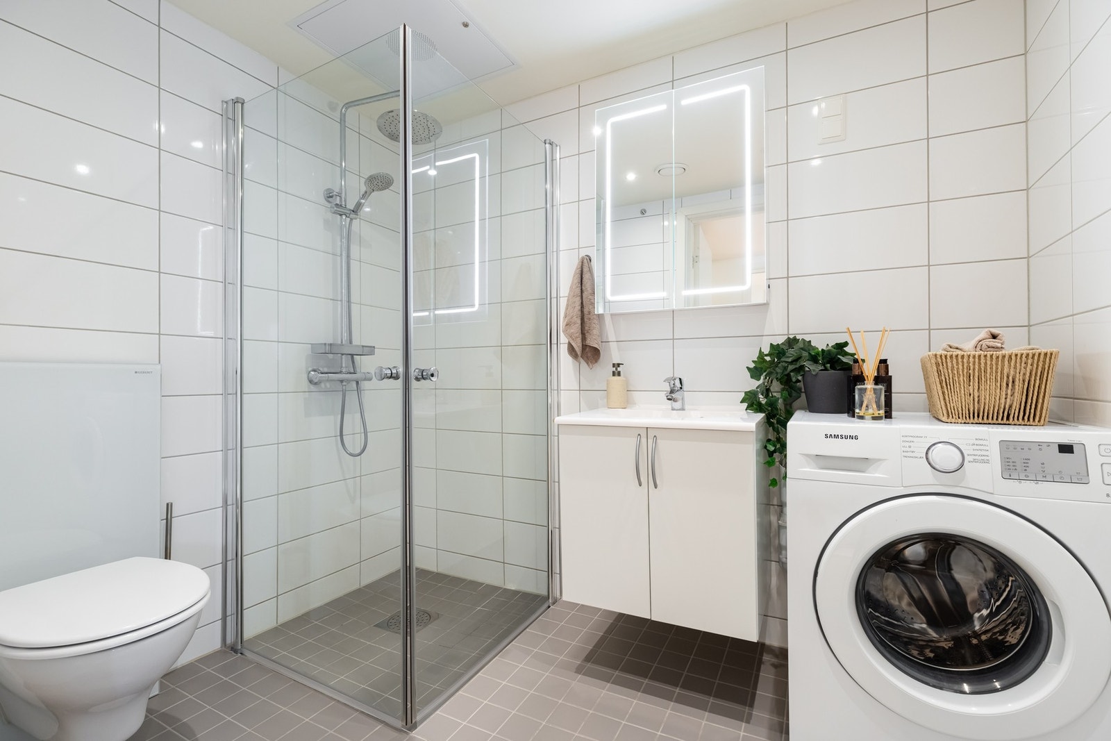 Boligens bad er bygget opp med grå fliser på gulv og lyse fliser på vegger. Det er downlights i himling og varme i gulv. Galleribilde