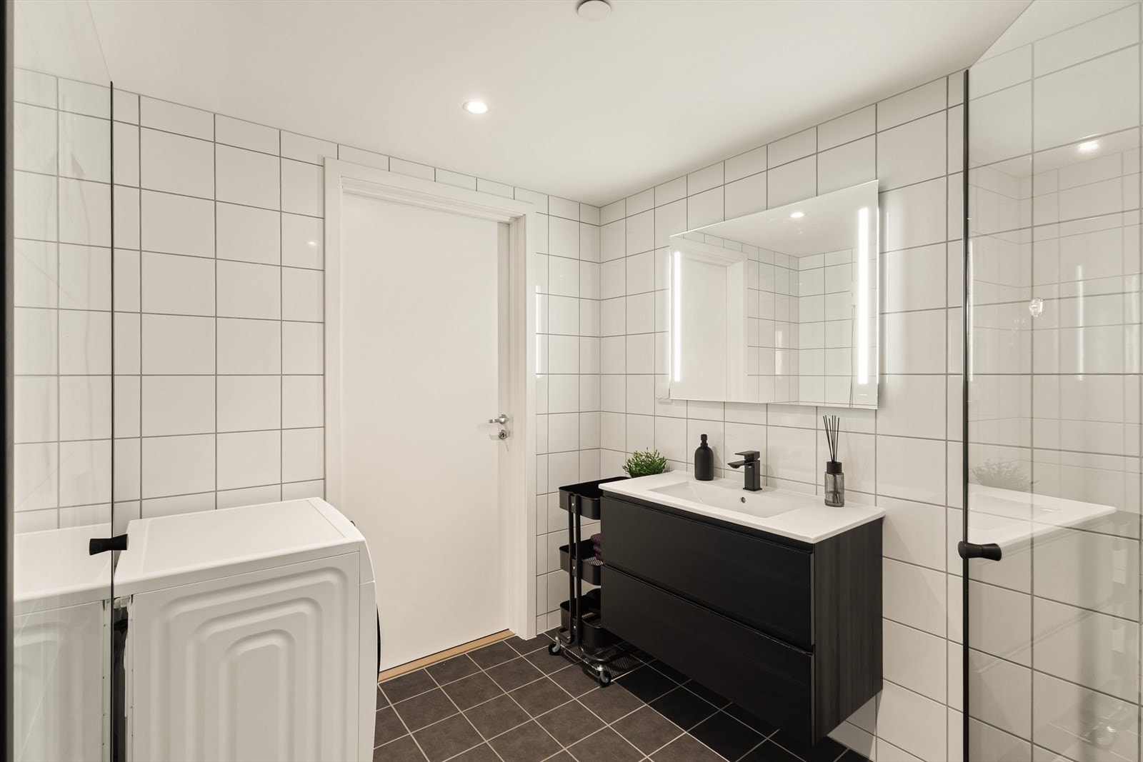 Et romslig bad med opplegg for vaskemaskin, og sorte, moderne detaljer på vask og i dusjsonen. Galleribilde