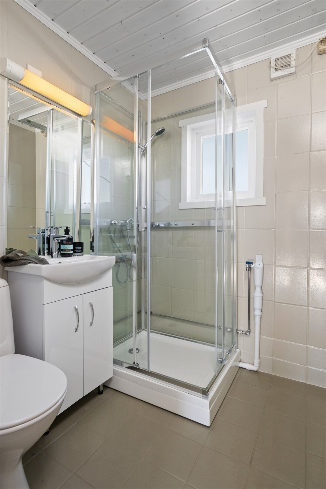 Badet er helfliselagt og med varmekabler i gulv. Baderomsinnredningen består av heldekkende servant med underskap og overhengende speil. Videre er det sokkeltoalett og nytt dusjkabinett. Galleribilde