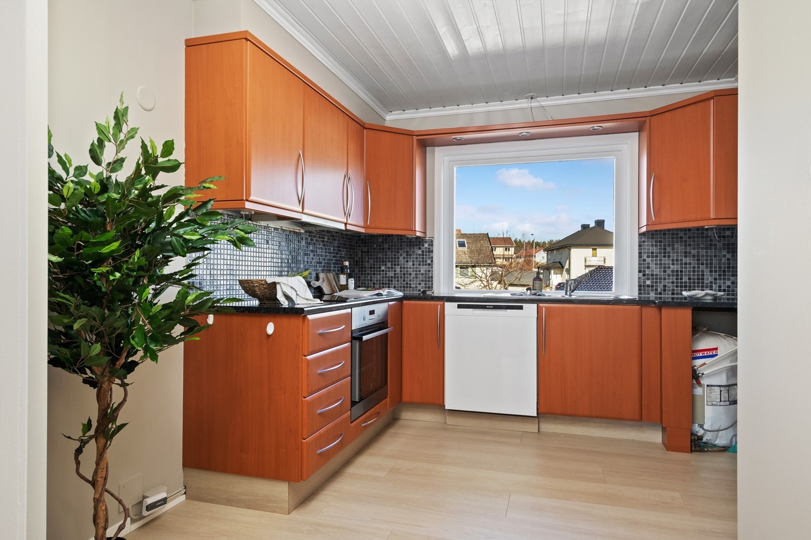 Kjøkkenet er et hyggelig rom som ligger i sammenheng med stuen. Innredningen har slette fronter og laminat benkeplater med fliser over. Galleribilde