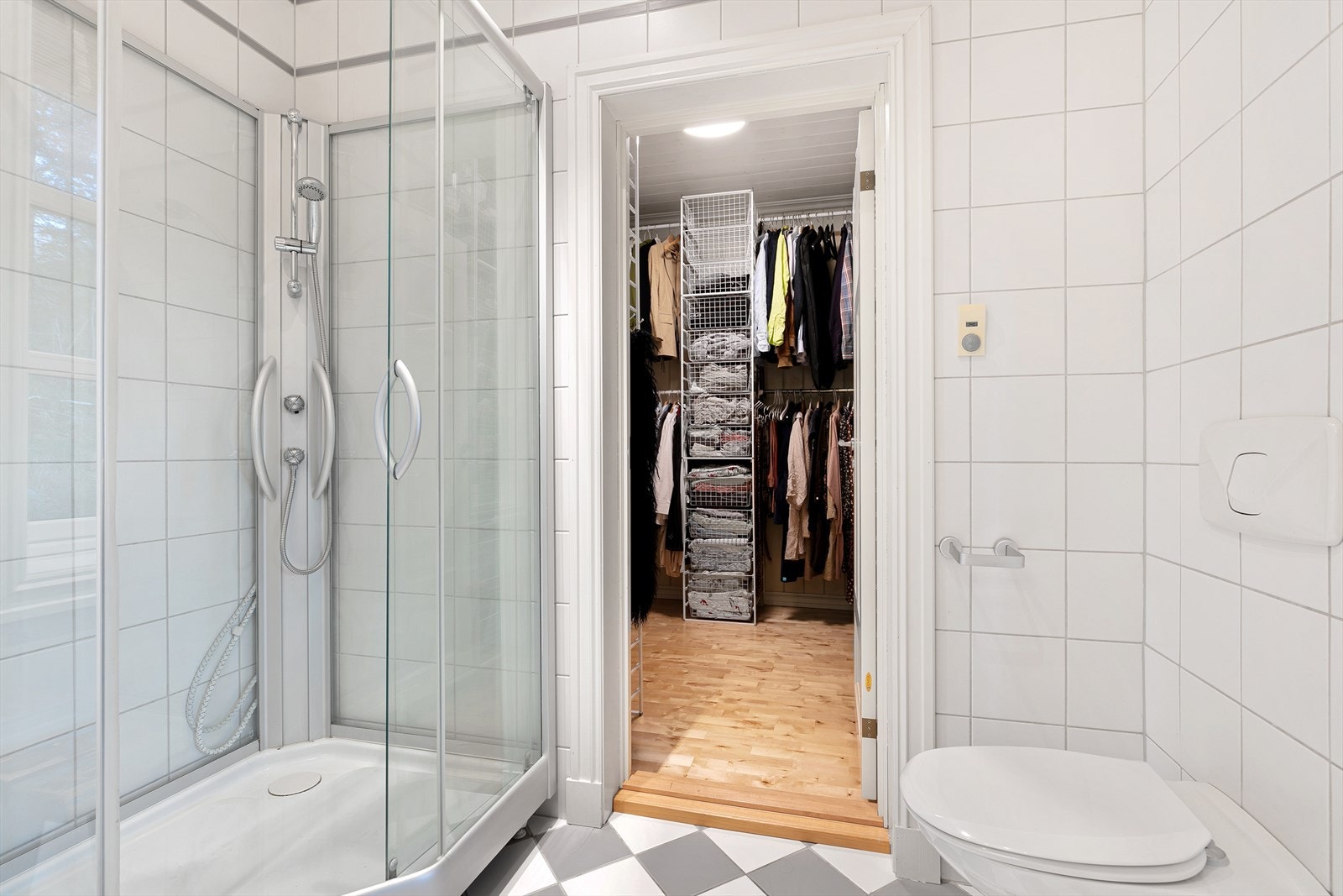 Det andre badet ligger i tilknytning til hovedsoverommet - en behagelig hverdagsluksus. Hvite veggfliser kombineres med sjakkmønstrede gulvfliser i hvitt og lysegrått. Downlights og gulvvarme er installert, og på badet er det dusjkabinett. Galleribilde