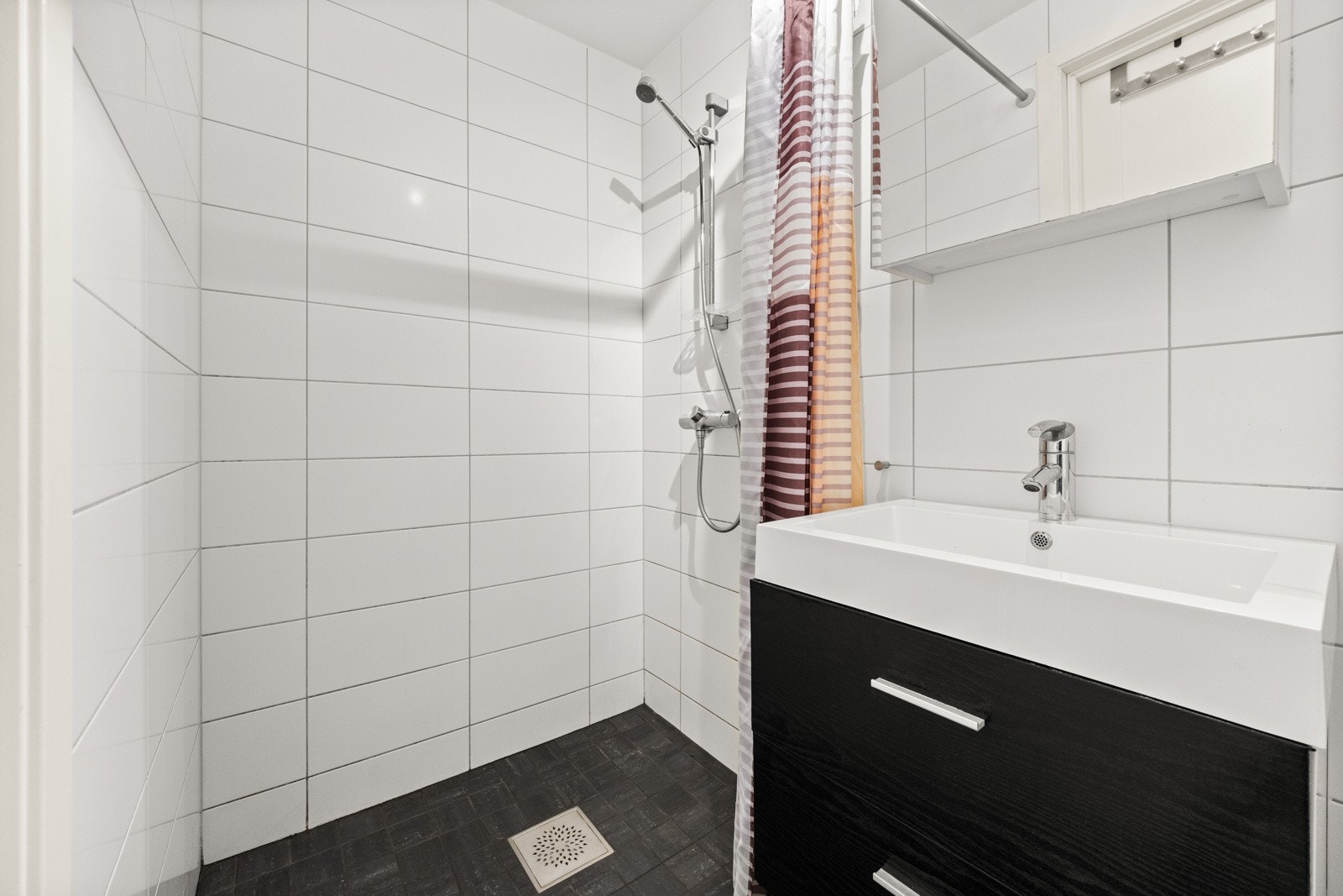 Badet i hybeldelen er utstyrt med et dusjhjørne, en enkel servantinnredning med underskap og overskap med speil, samt toalett. Det er også en praktisk nisje med plass til vaskemaskin og overskap for oppbevaring. Galleribilde