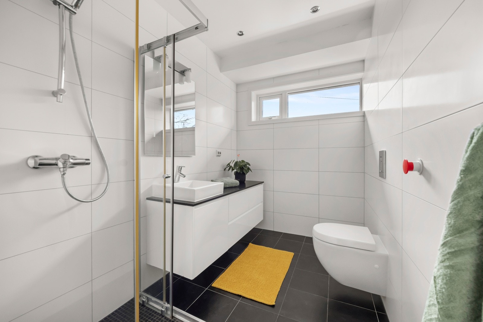 Bad nr. 2 i 2. etasje inneholder et dusjhjørne med skyvedører i glass, servant med speil, en funksjonell innredning med underskap og skuffer, stor benkeplate i naturstein samt et vegghengt toalett. Galleribilde