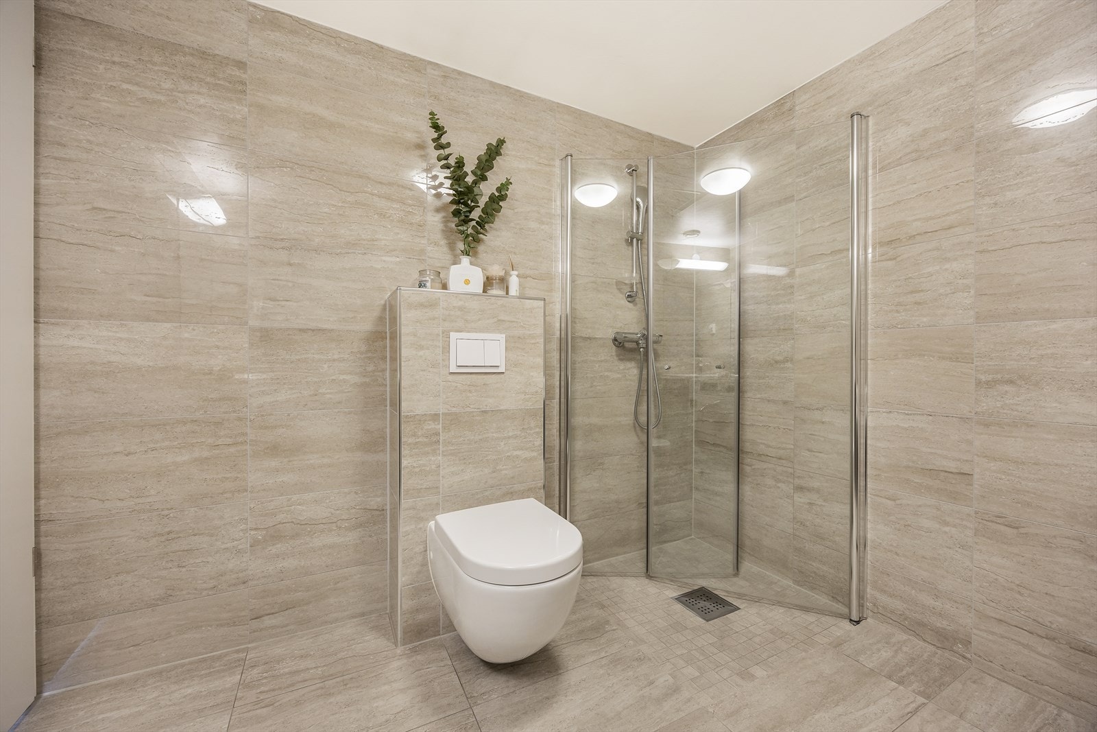 Badet er utstyrt med dusjhjørne med innfellbare glassvegger, vegghengt wc og servantinnredning med skuffer Galleribilde