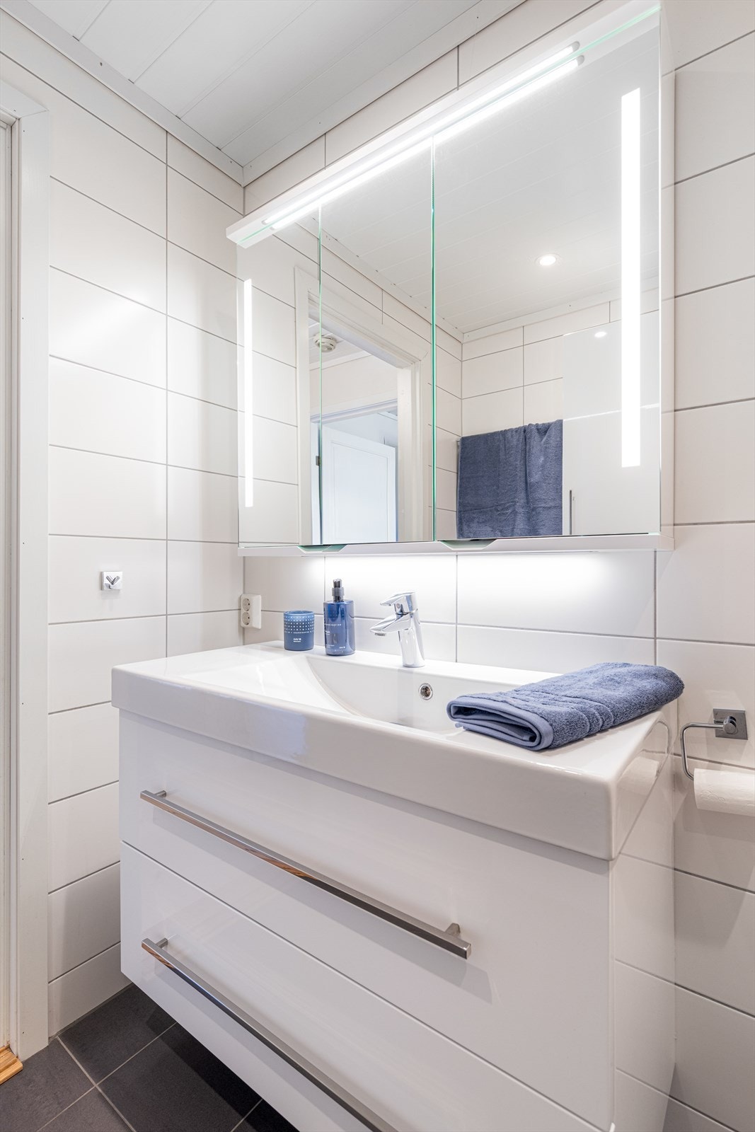 Badet er innredet med vegghengt toalett og dusjnisje med vegger i herdet glass. Samt servantinnredning med underskuffer og overskap med speil og overlys. Det er avtrekksvifte i tak. Galleribilde