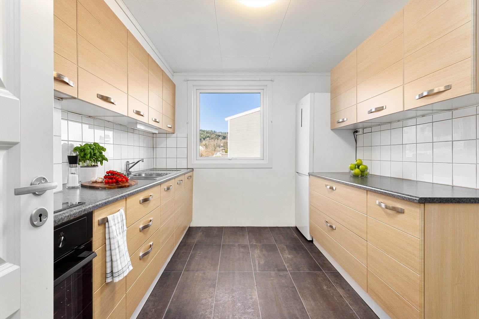 Pent kjøkken med glatte fronter, flislagt over kjøkkebenk og benkeplate i laminat Galleribilde