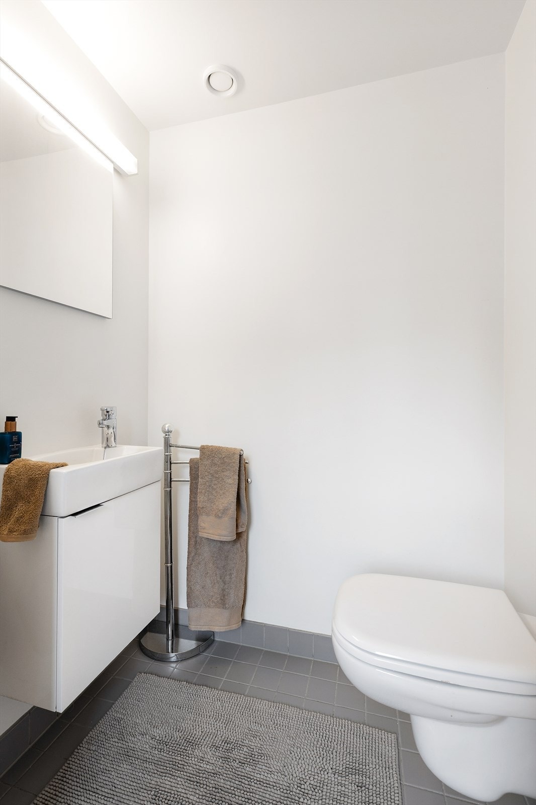 Toalettrom fra byggeår. Flislagt gulv. Vegghengt servantskap med dør. Ovenpåliggende servant med ett-greps armatur. Speil og overlys med stikkontakt på vegg over servant. Vegghengt toalett med innebygd sisterne. Avtrekksventil i himling. Galleribilde