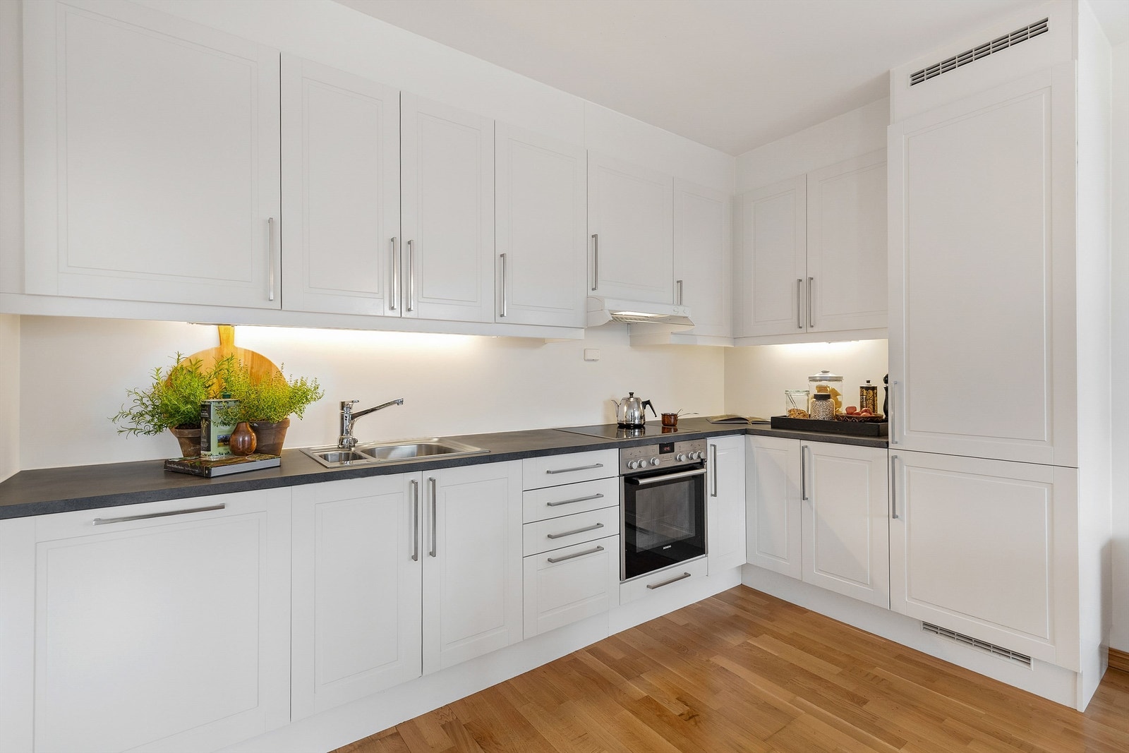 Integrerte hvitevarer. Kjøleskap med frysedel, oppvaskmaskin og ovn. Nedfelt keramisk platetopp. Vegghengt ventilator. Komfyrvakt. Galleribilde