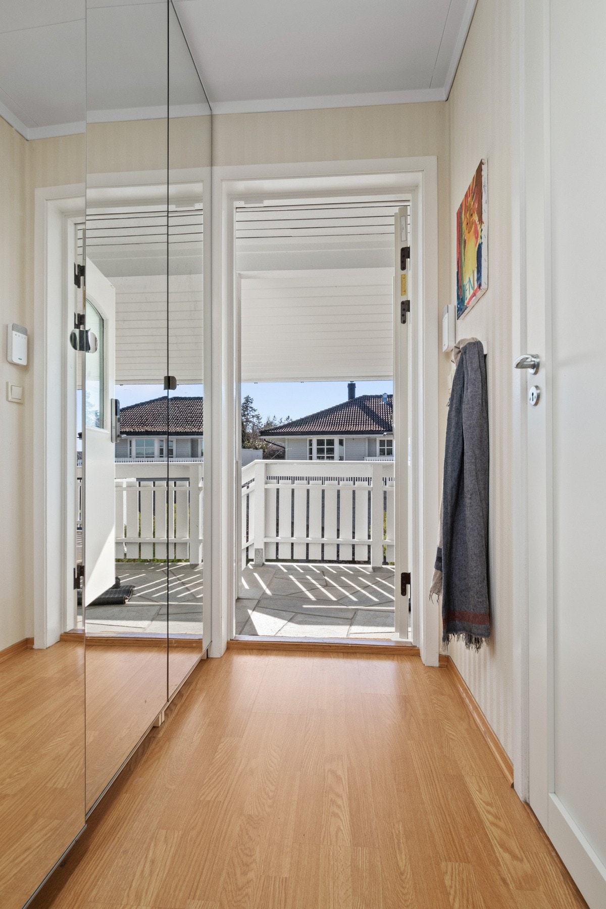 Pen entré med lyse, tapetserte vegger og parkettgulv. Yttertøyet ryddes enkelt bort i en bred rekke med garderobeskap med speilfronter. Galleribilde