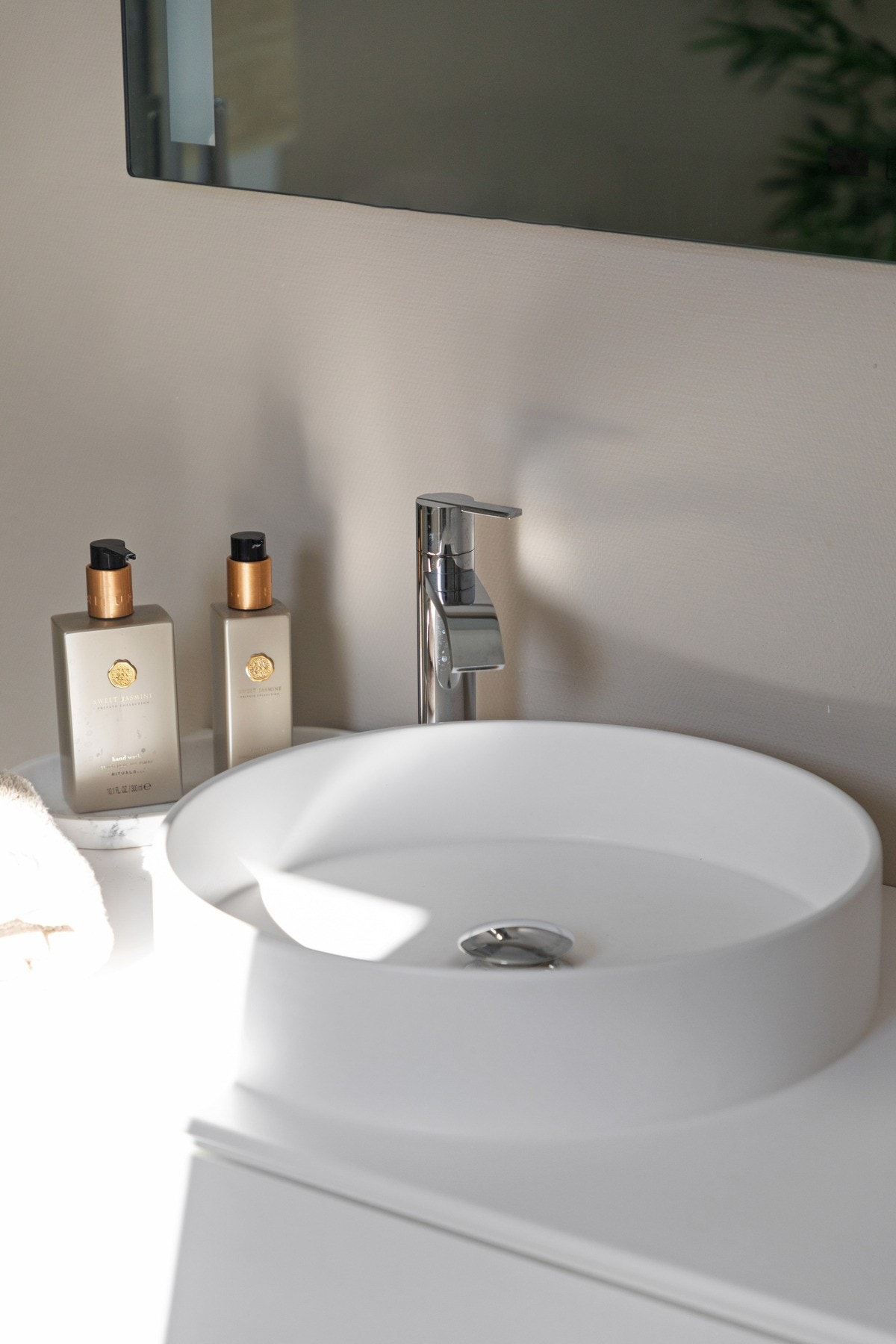 Baderomsinnredningen har lyse, glatte fronter og består av en toppmontert, rund servant på en skuffeseksjon og et stort speil med integrert belysning. Galleribilde