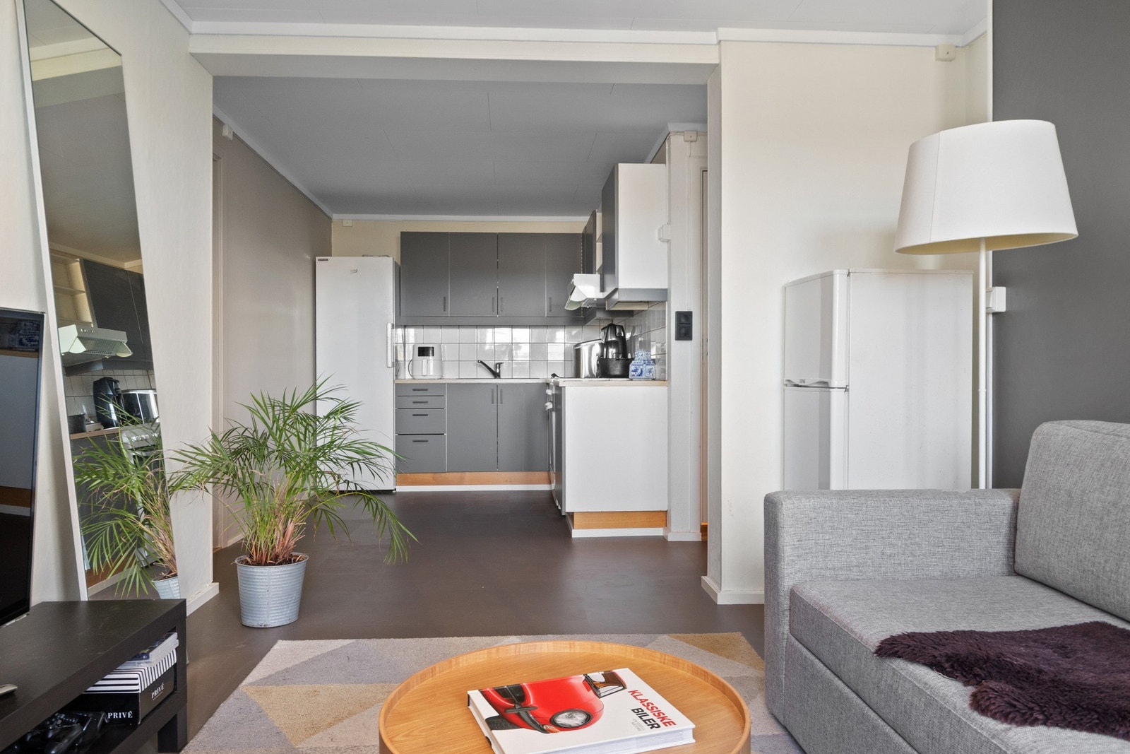 Det åpne rommet som utgjør stue og kjøkken har hvit- og gråmalte vegger, og på gulvet er det grått belegg og elektrisk gulvvarme. Galleribilde